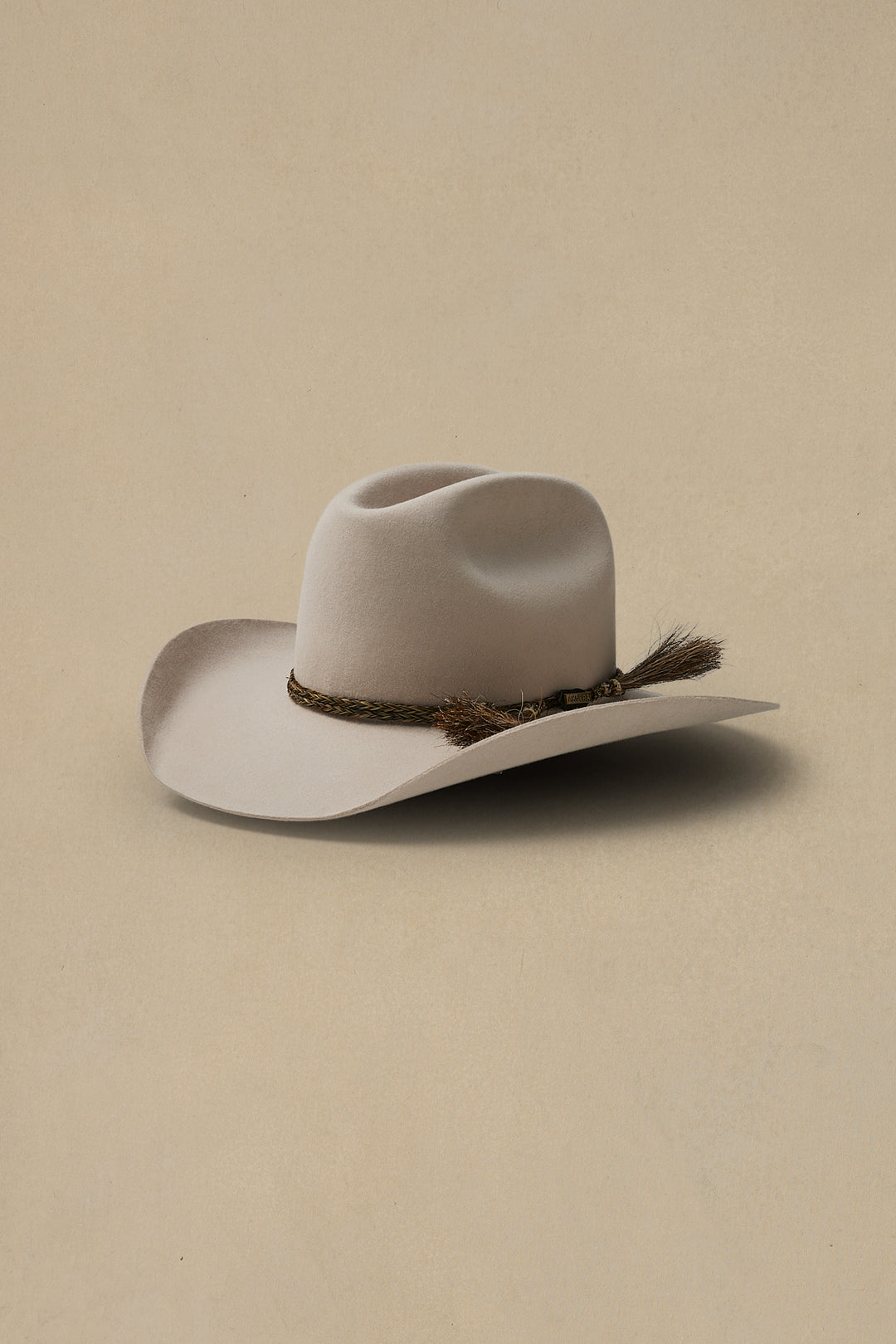 Light sand colored felt cowboy hat with braided hatband and feather accent on neutral beige background