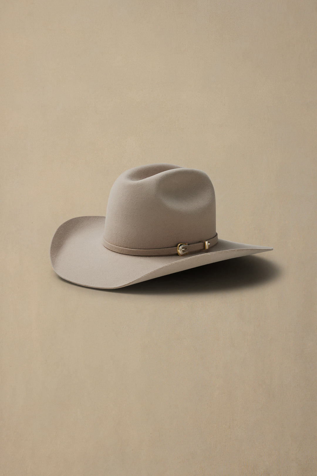Light sand colored rabbit fur felt cowboy hat with cattleman crown and leather hatband on neutral beige background