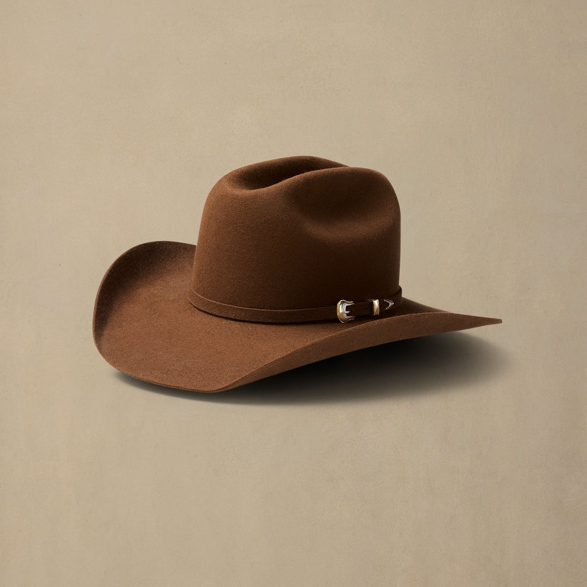 Brown rabbit fur cowboy hat with cattleman crown and decorative band, displayed against neutral beige background