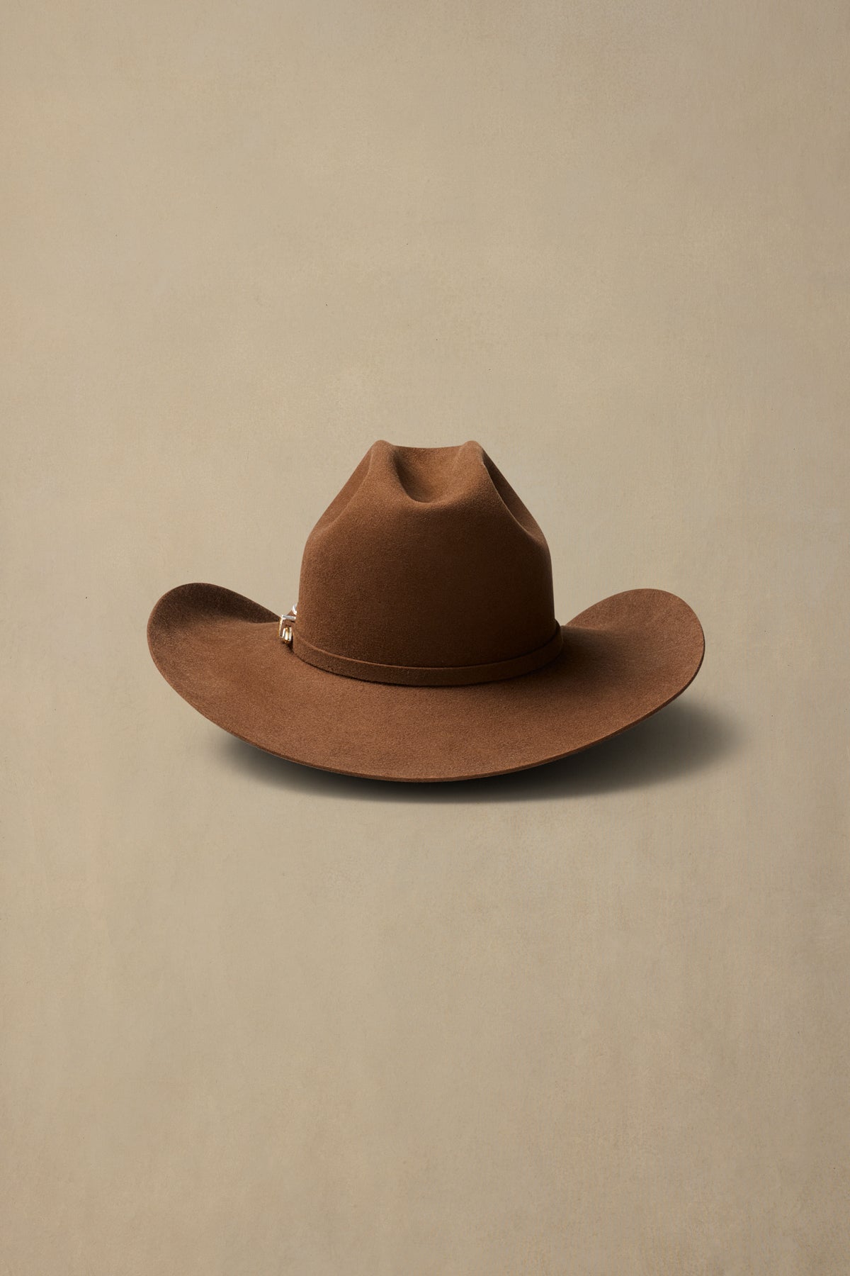 Brown fur felt cowboy hat with wide brim and cattleman crown displayed against neutral beige background