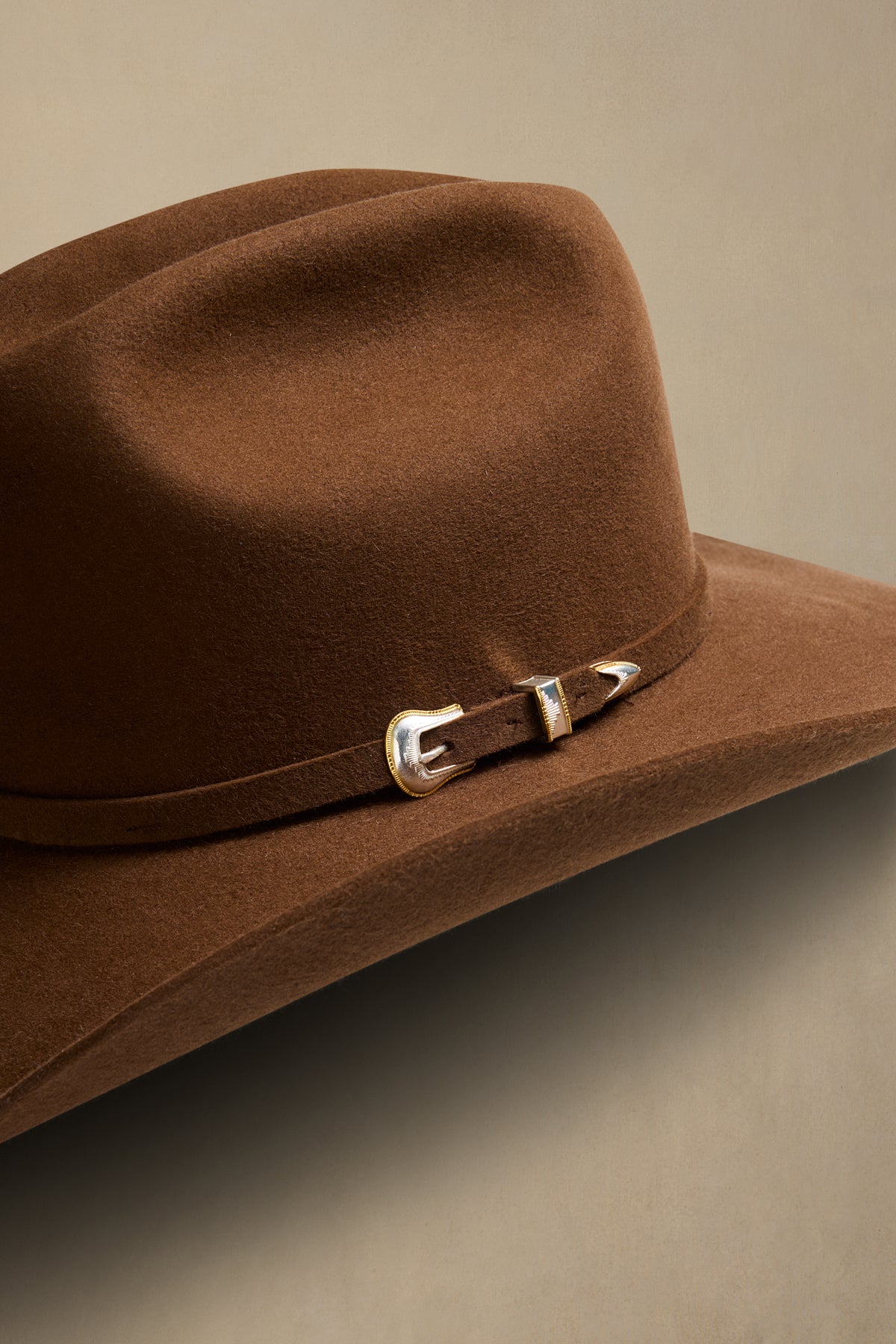 Brown fur felt cowboy hat with silver buckle band detail on neutral background
