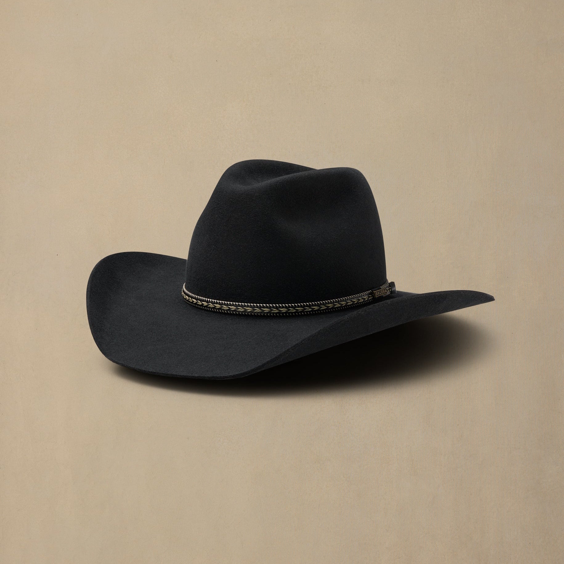 Black cowboy hat with decorative band on neutral beige background, side view