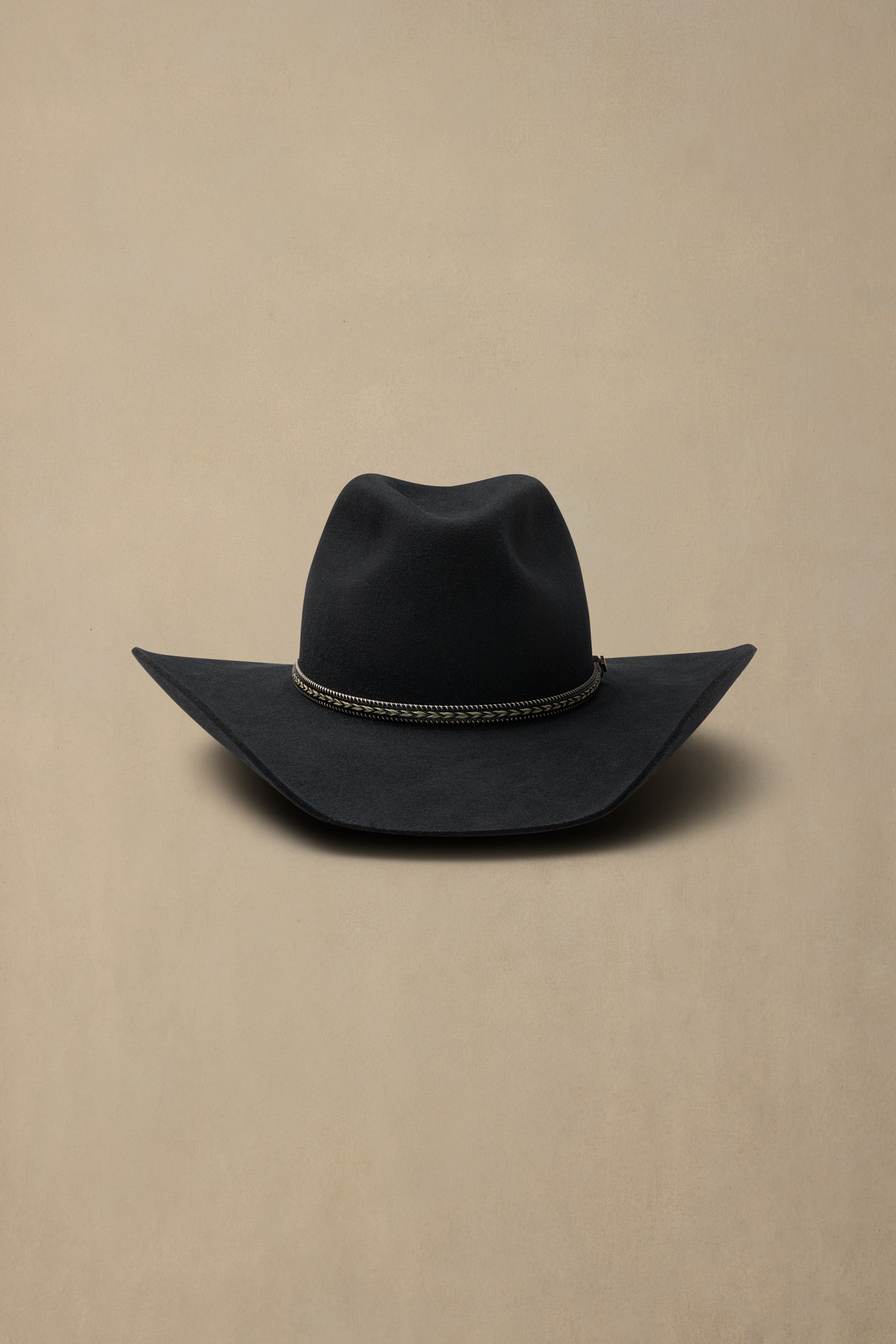 Black cowboy hat with decorative band on beige background