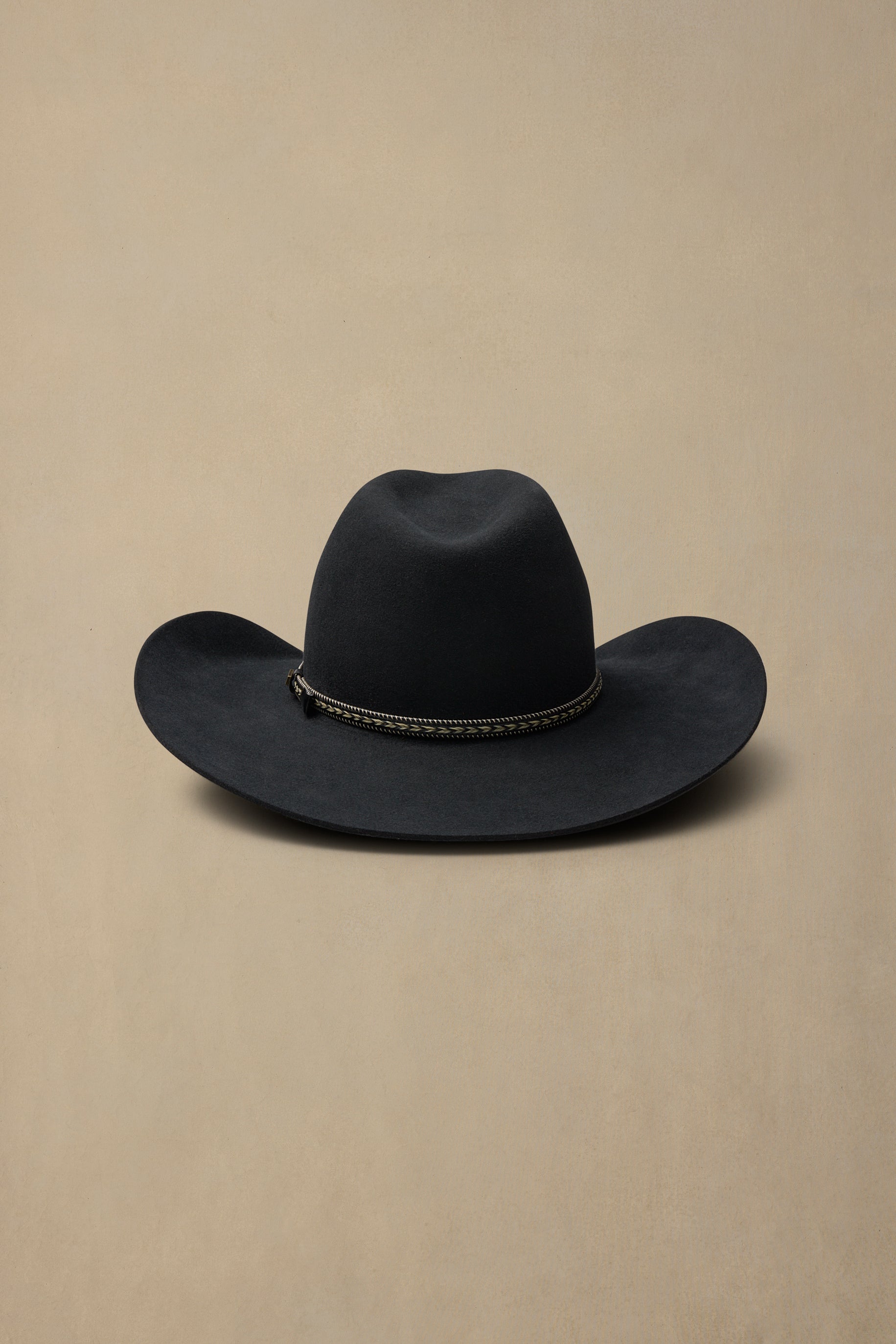 Black fur felt cowboy hat with decorative braided band on neutral beige background
