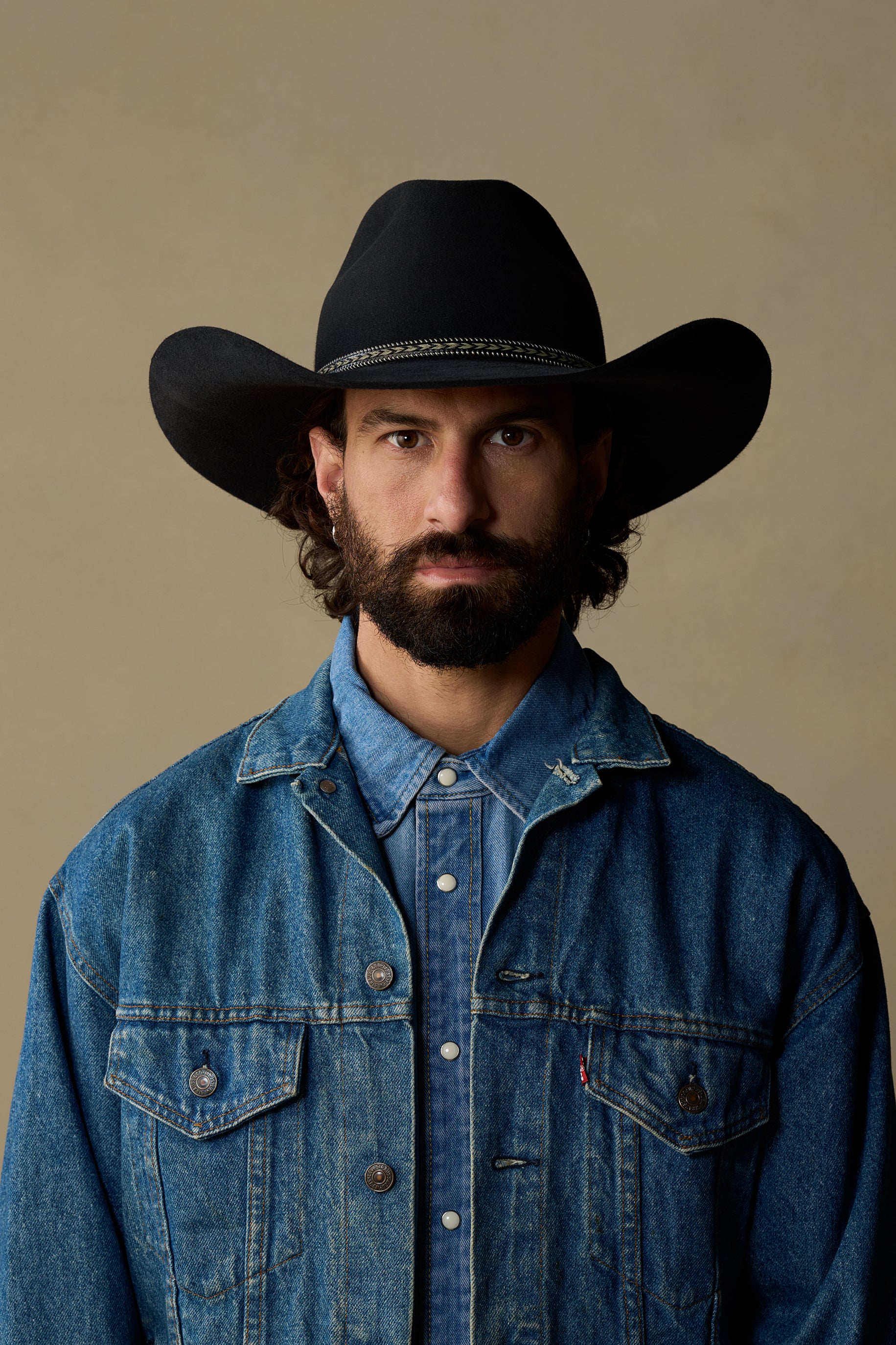 Black cowboy hat with wide brim worn by man in denim jacket against neutral background