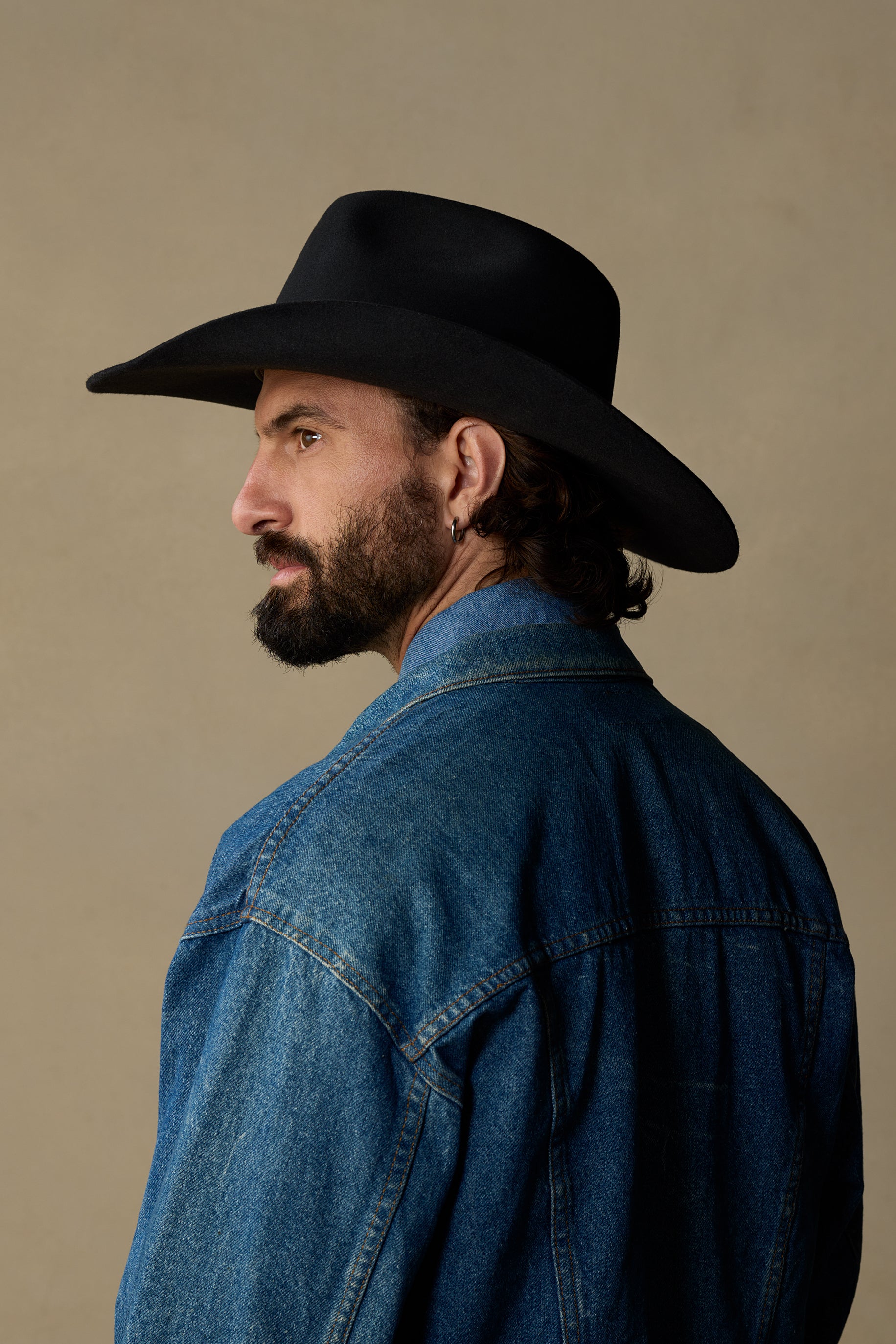 Black Dusty Dawn cowboy hat on man wearing denim shirt, side profile view against tan background