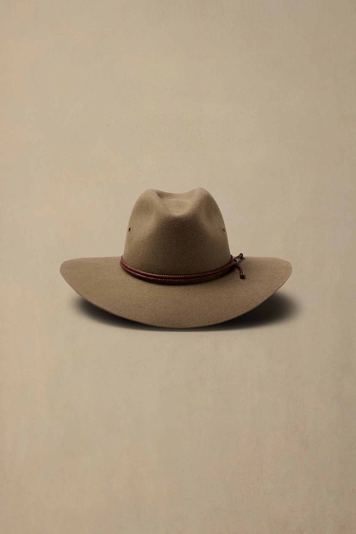 Tan rabbit fur felt traveller cowboy hat with burgundy rope band on cream background