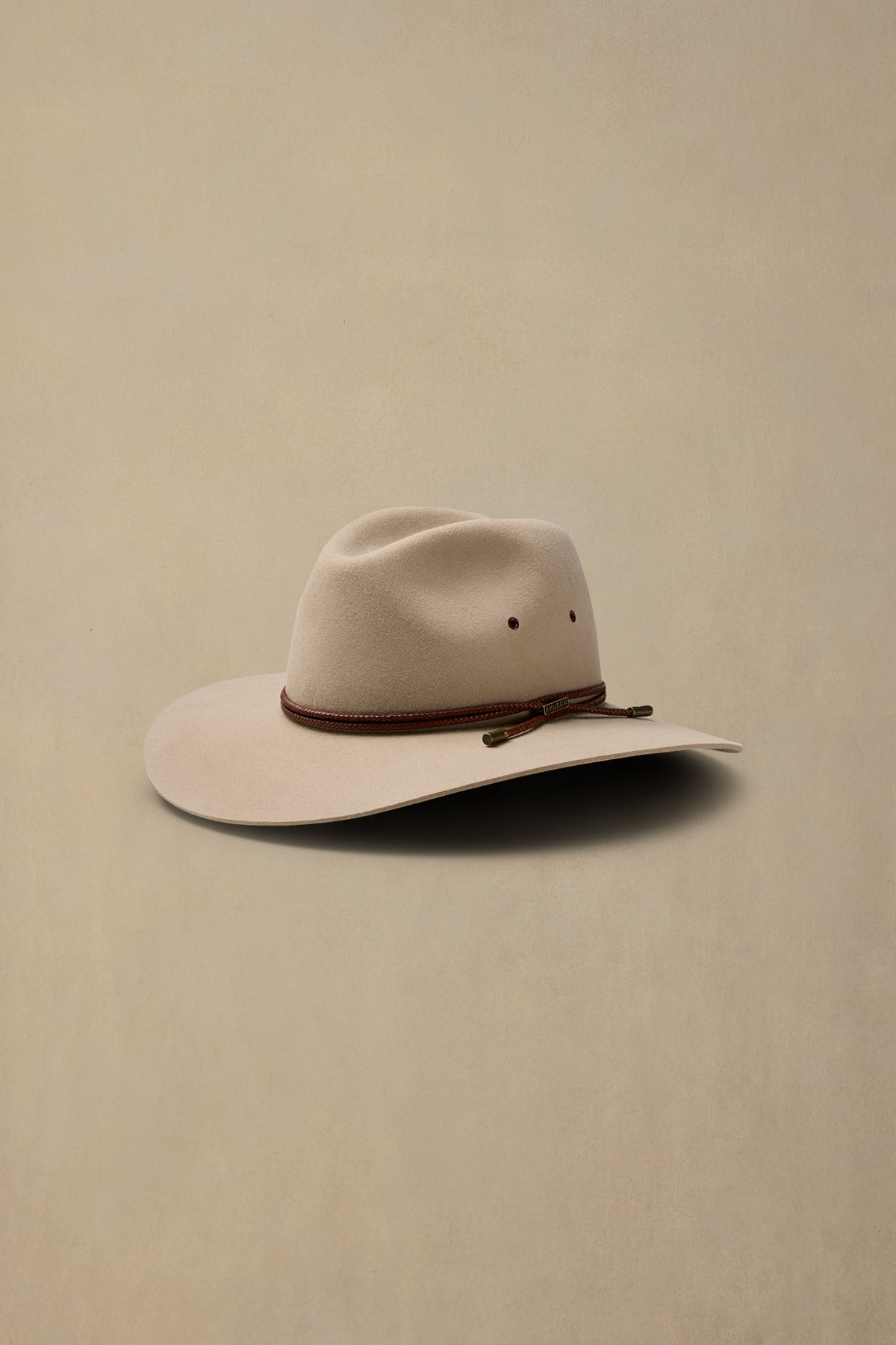 Cream rabbit fur cowboy hat with brown braided band and decorative ties displayed against neutral background