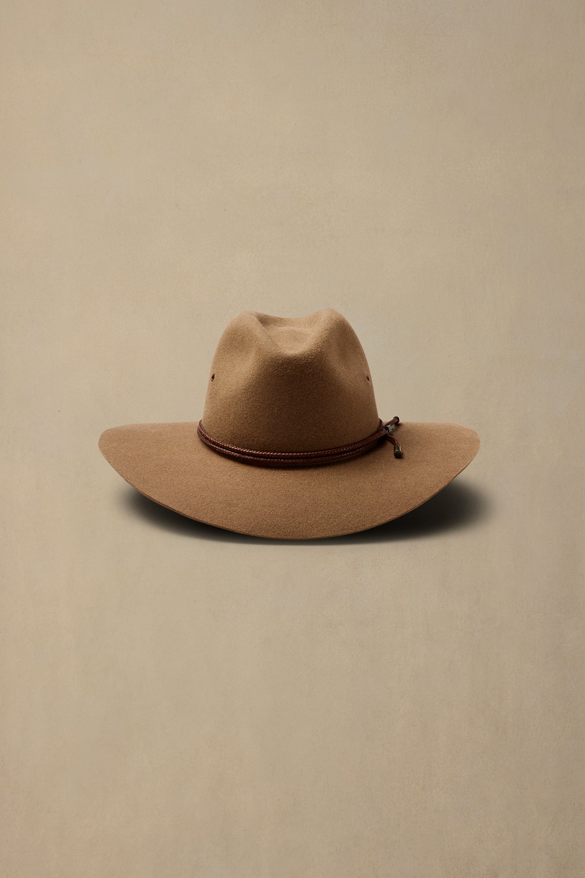 Tan rabbit fur felt cowboy hat with brown braided band on neutral background