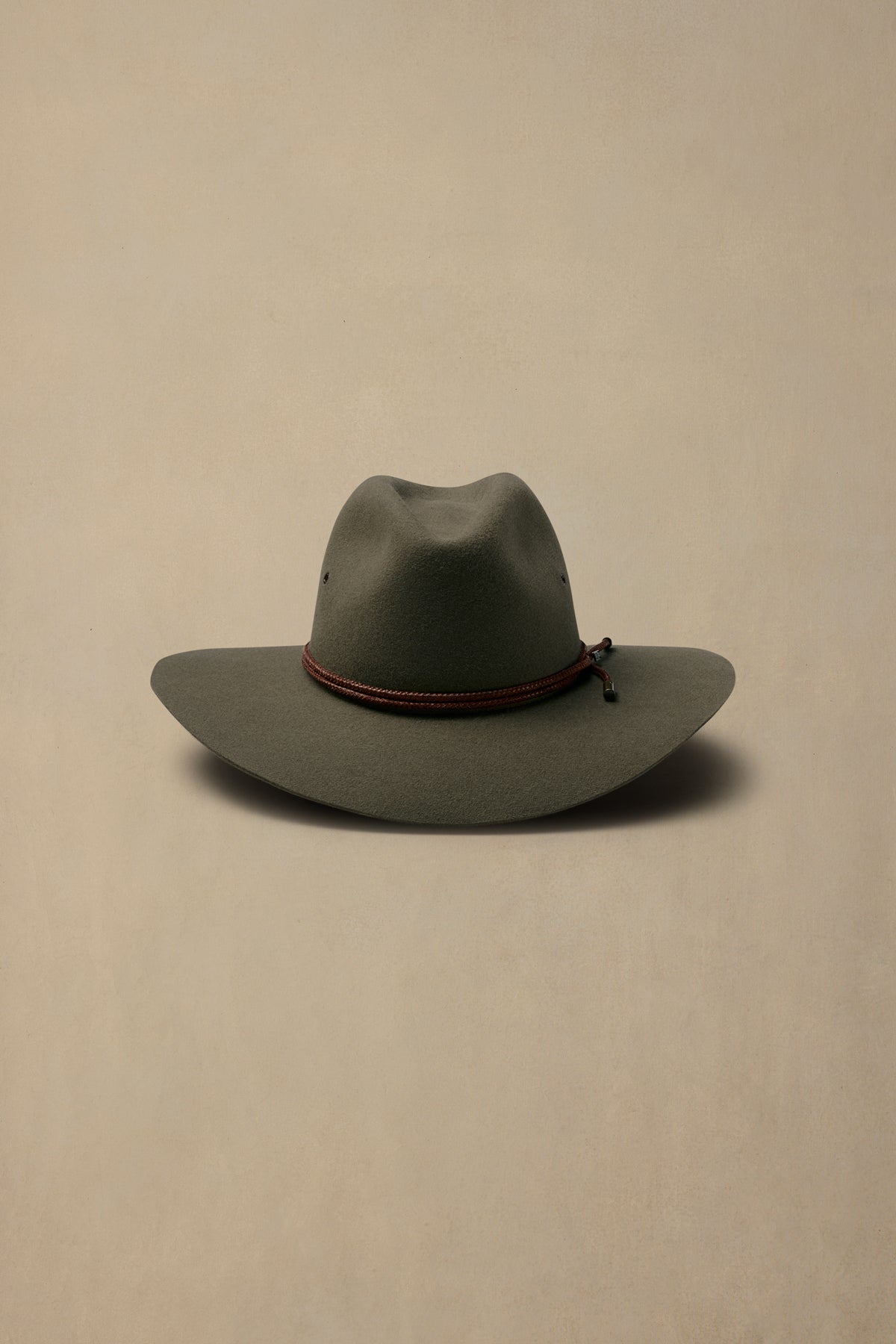 Sage green rabbit fur felt cowboy hat with burgundy cord band against neutral beige background
