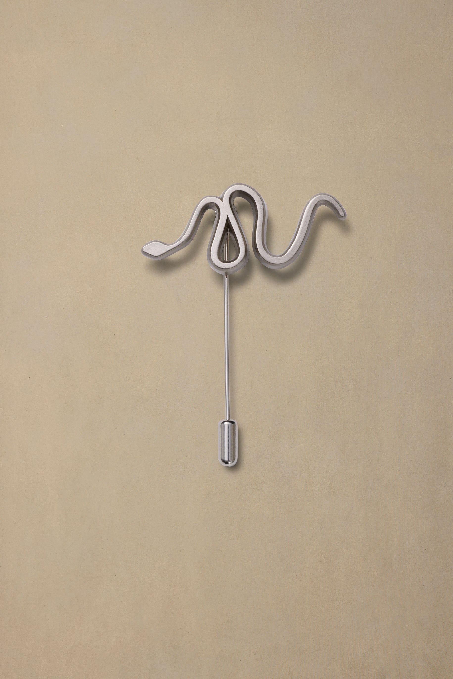 Silver serpent-shaped pin with curved coils on beige background, pewter finish with hanging post