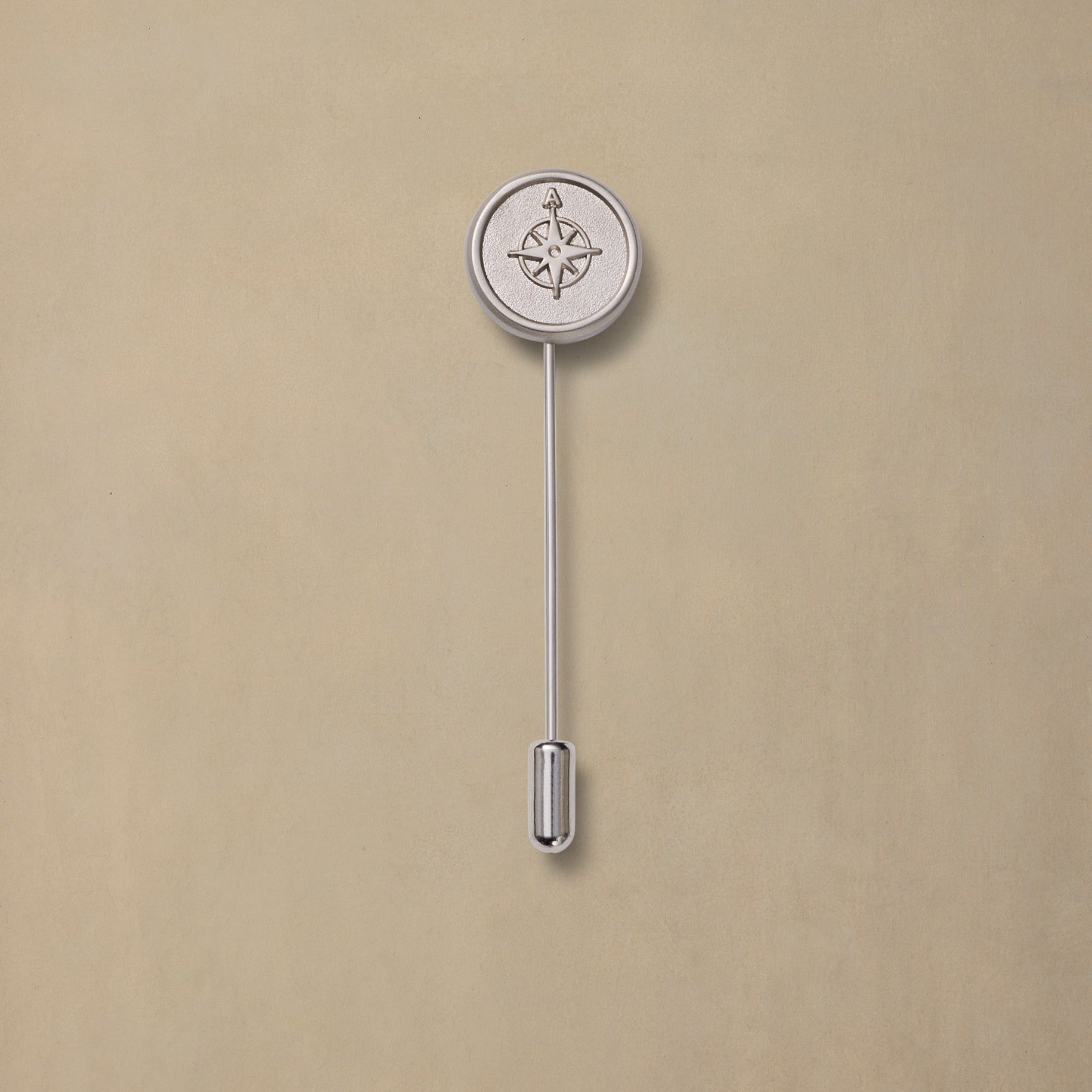 Silver compass rose lapel pin with long stem on beige background