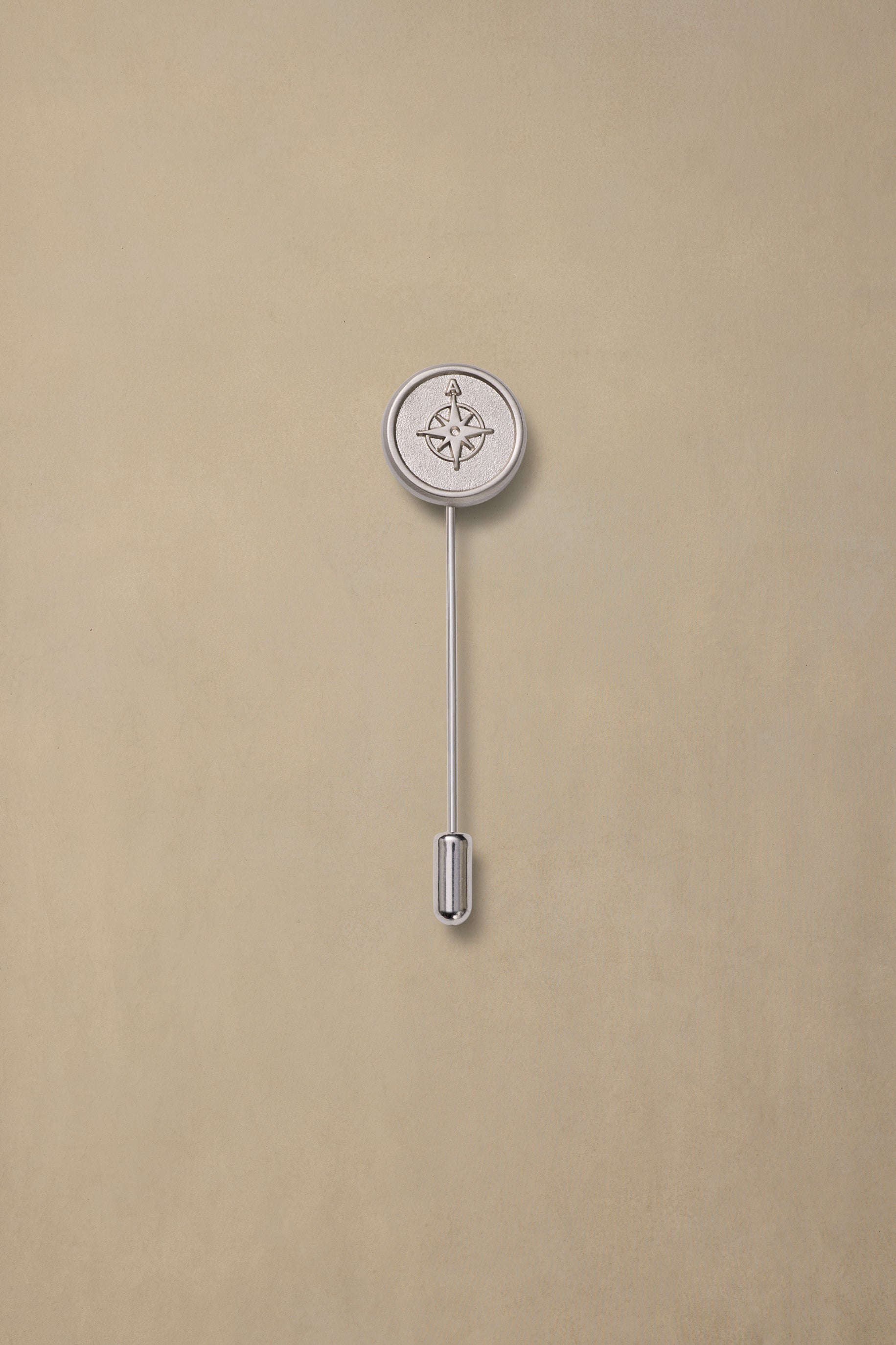 Silver compass rose pin with long stem on beige background