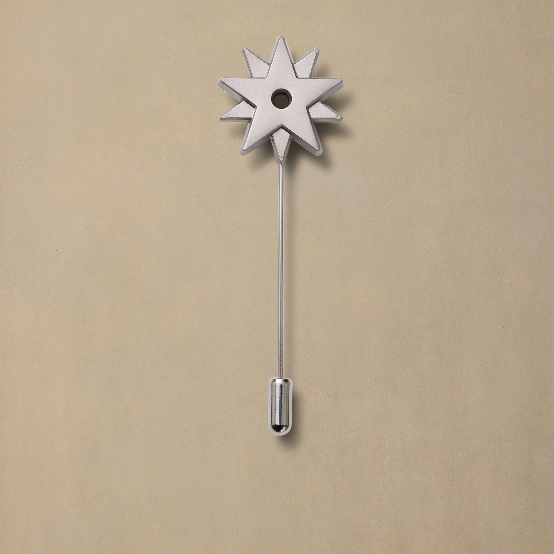 Pewter spur pin with eight-pointed star head and long stem on beige background