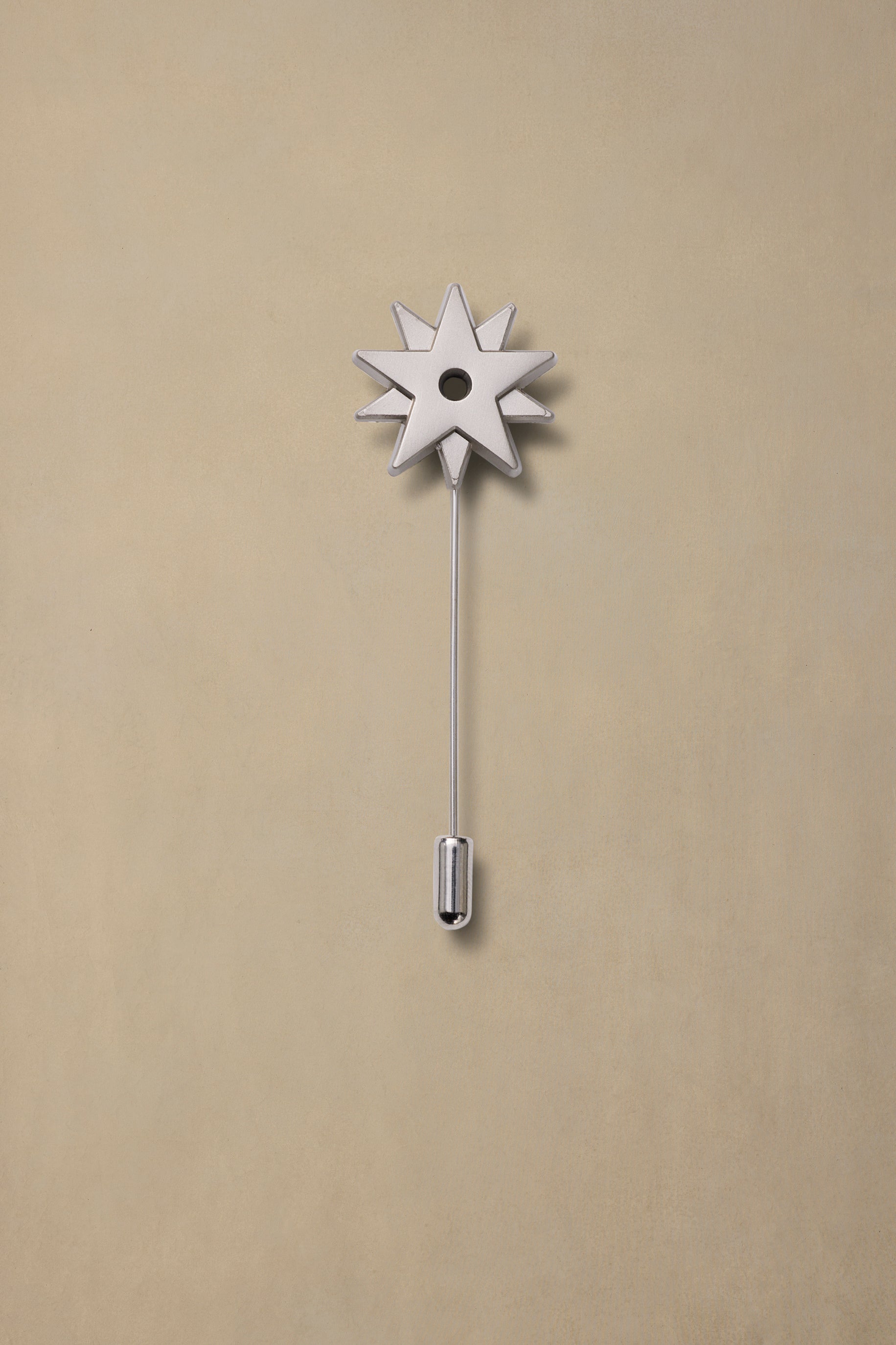 Pewter spur pin with eight-pointed star head and long stem on beige background