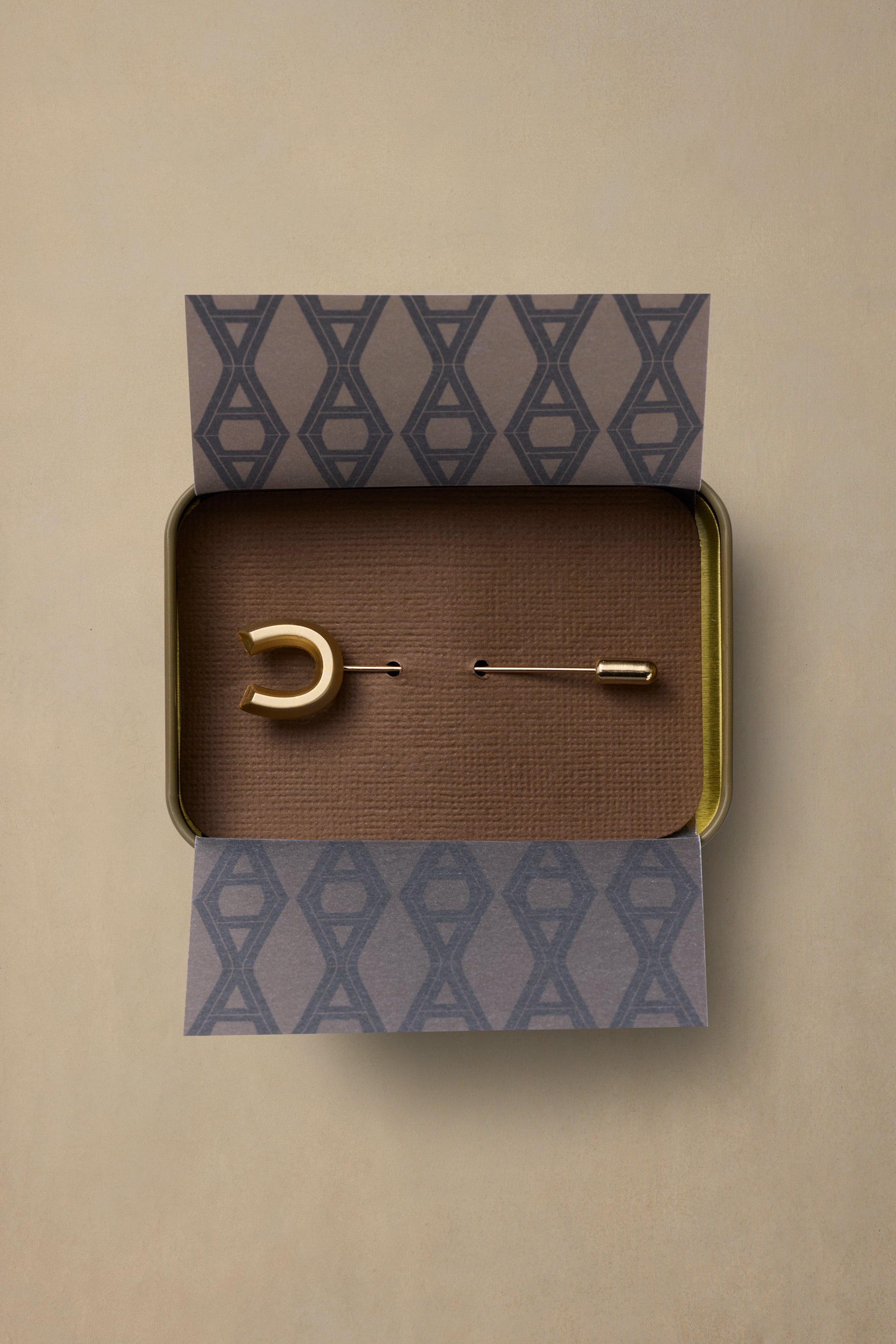 Lucky Brass pin with crescent and bar design in gold on brown textured box with patterned tissue wrap