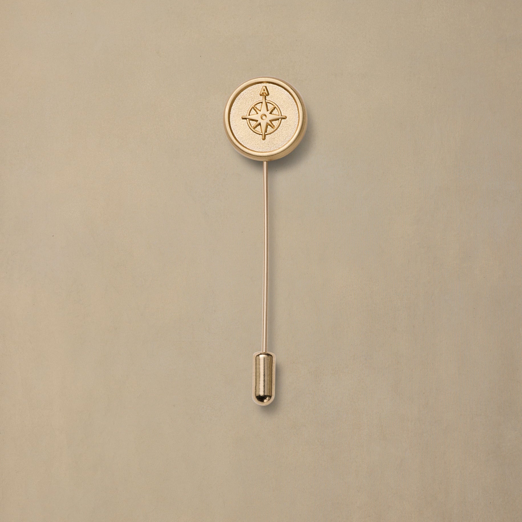 Gold compass rose pin with long stem on beige background, minimalist nautical design