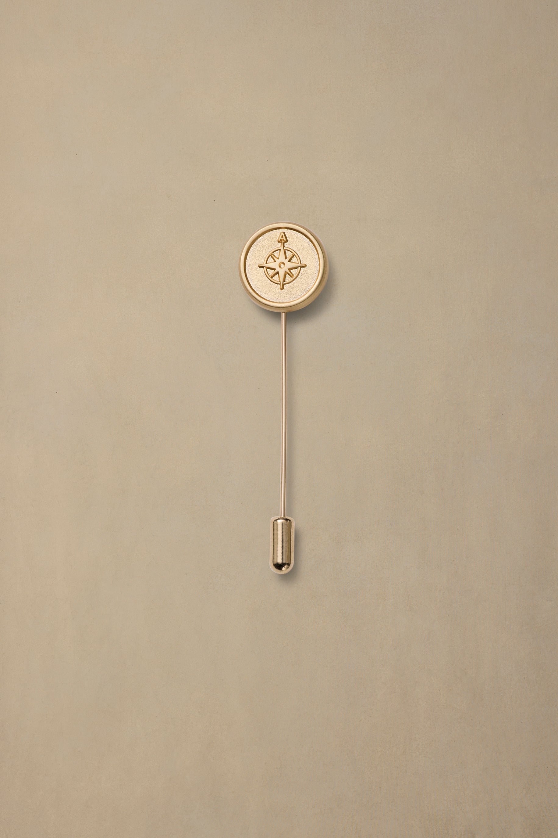 Gold compass rose pin with thin stem on neutral beige background