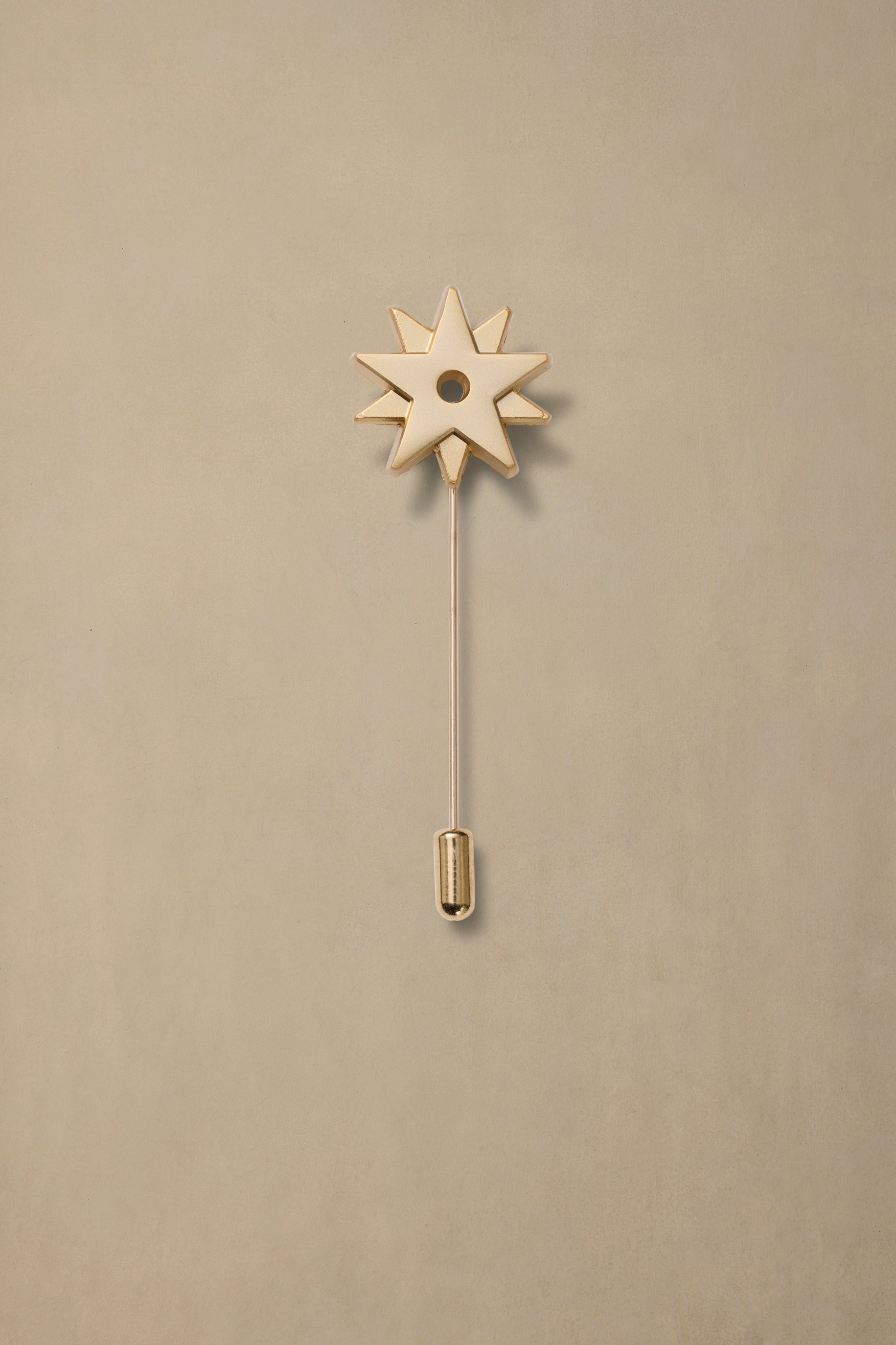 Polished brass spur pin with star-shaped head and pointed backing on cream background