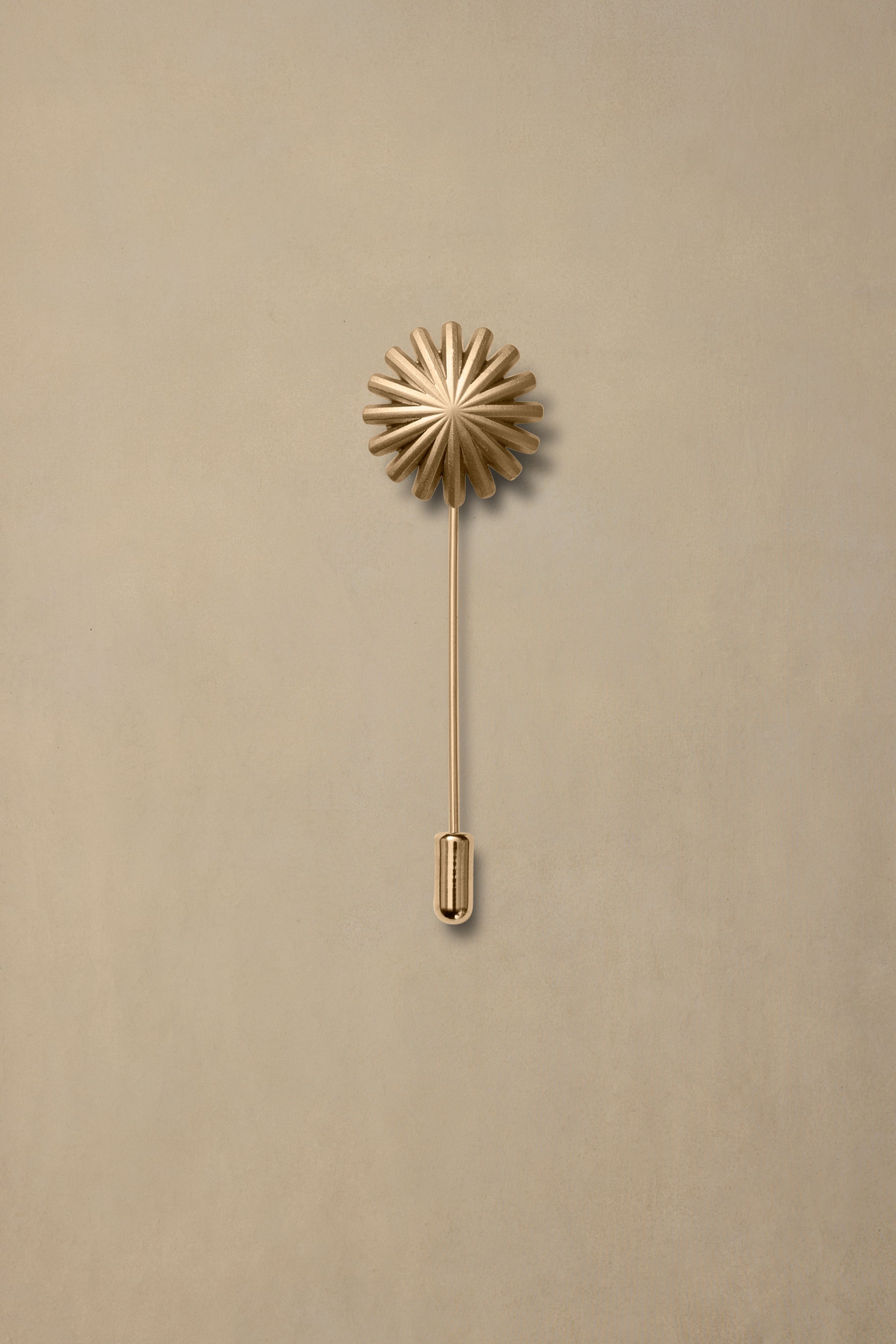 Brass starburst lapel pin with long stem on neutral beige background
