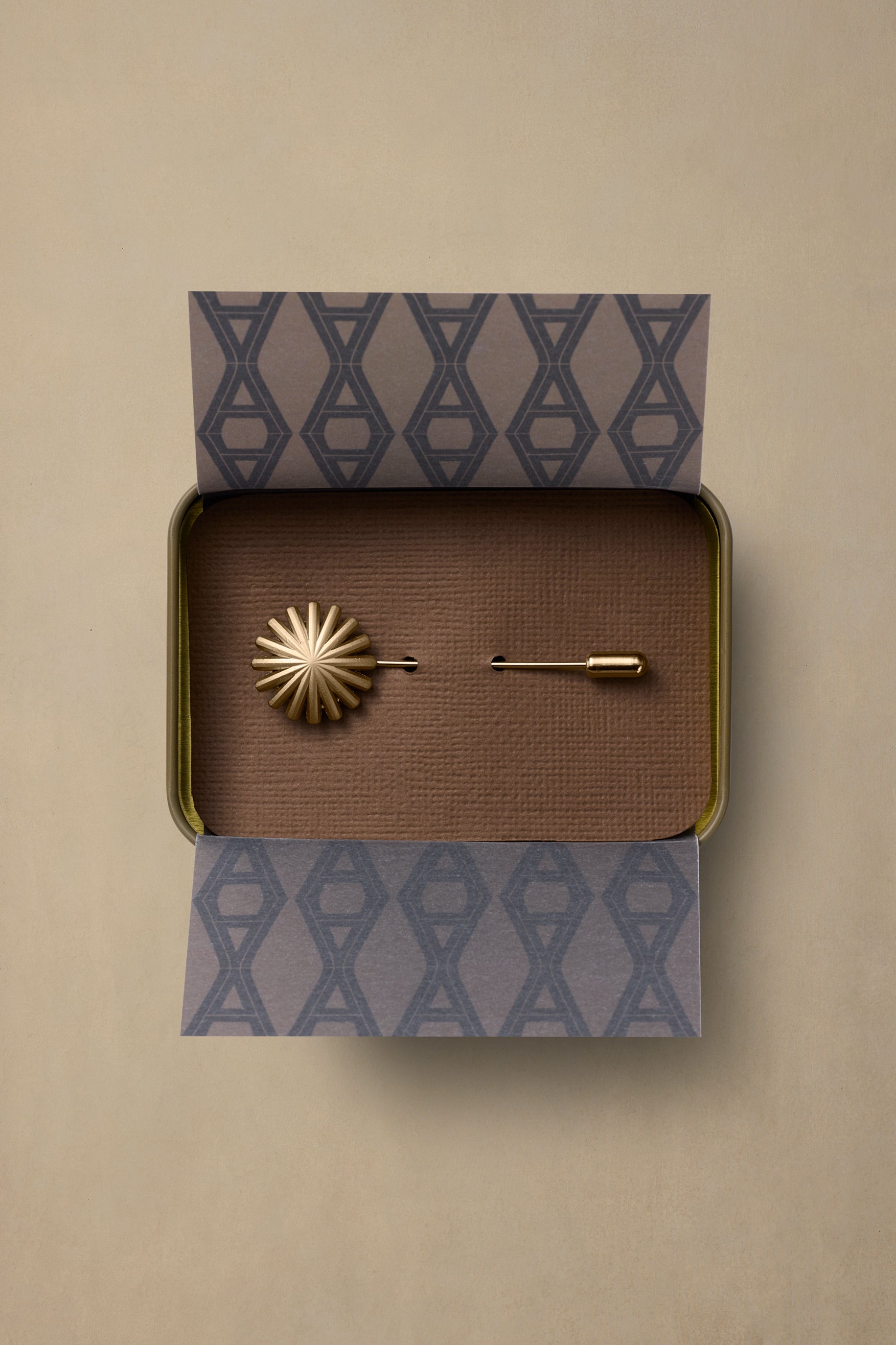 Gold starburst brass pin in branded box with patterned tissue paper on neutral background