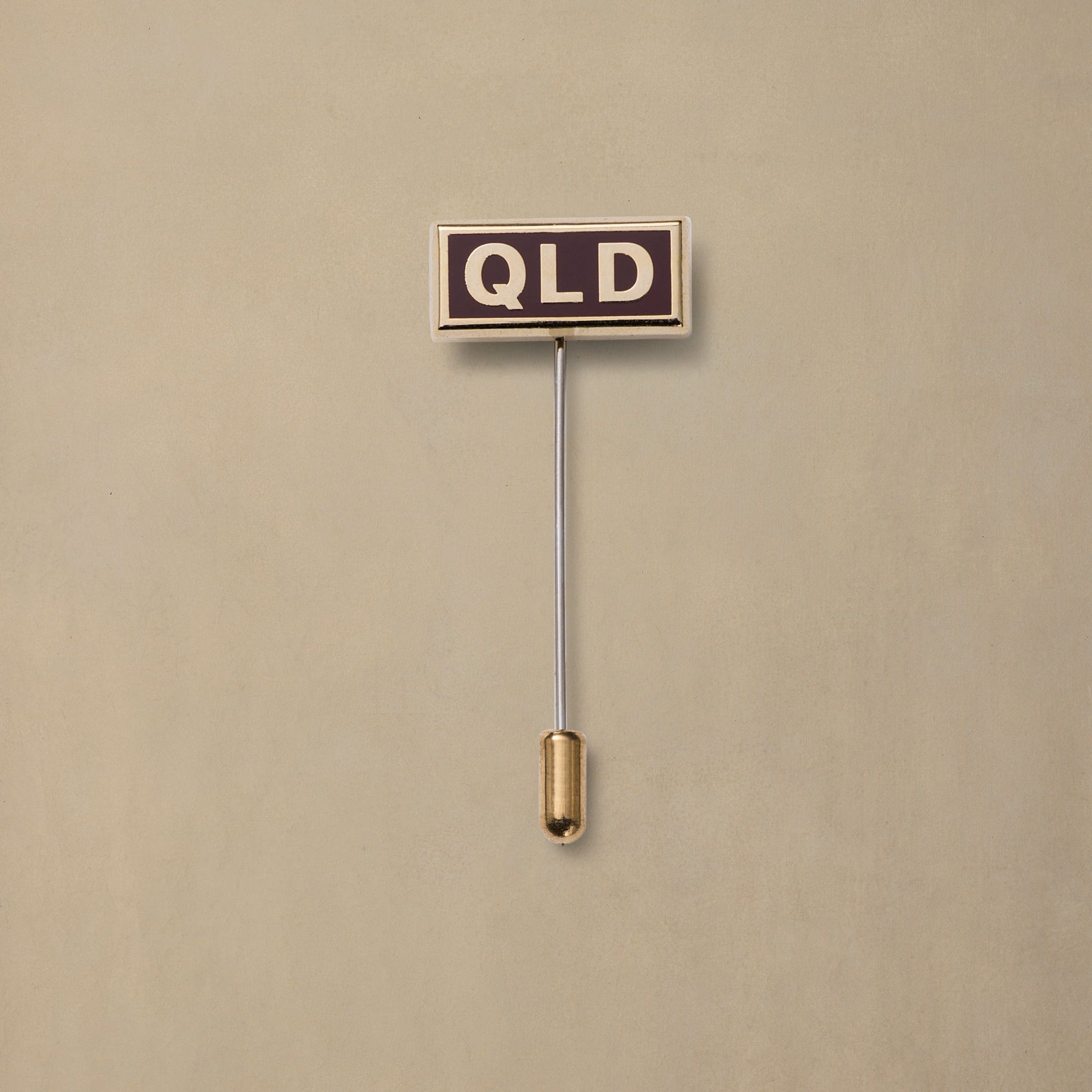 QLD state pin badge with dark enamel face and gold-tone stem on neutral background