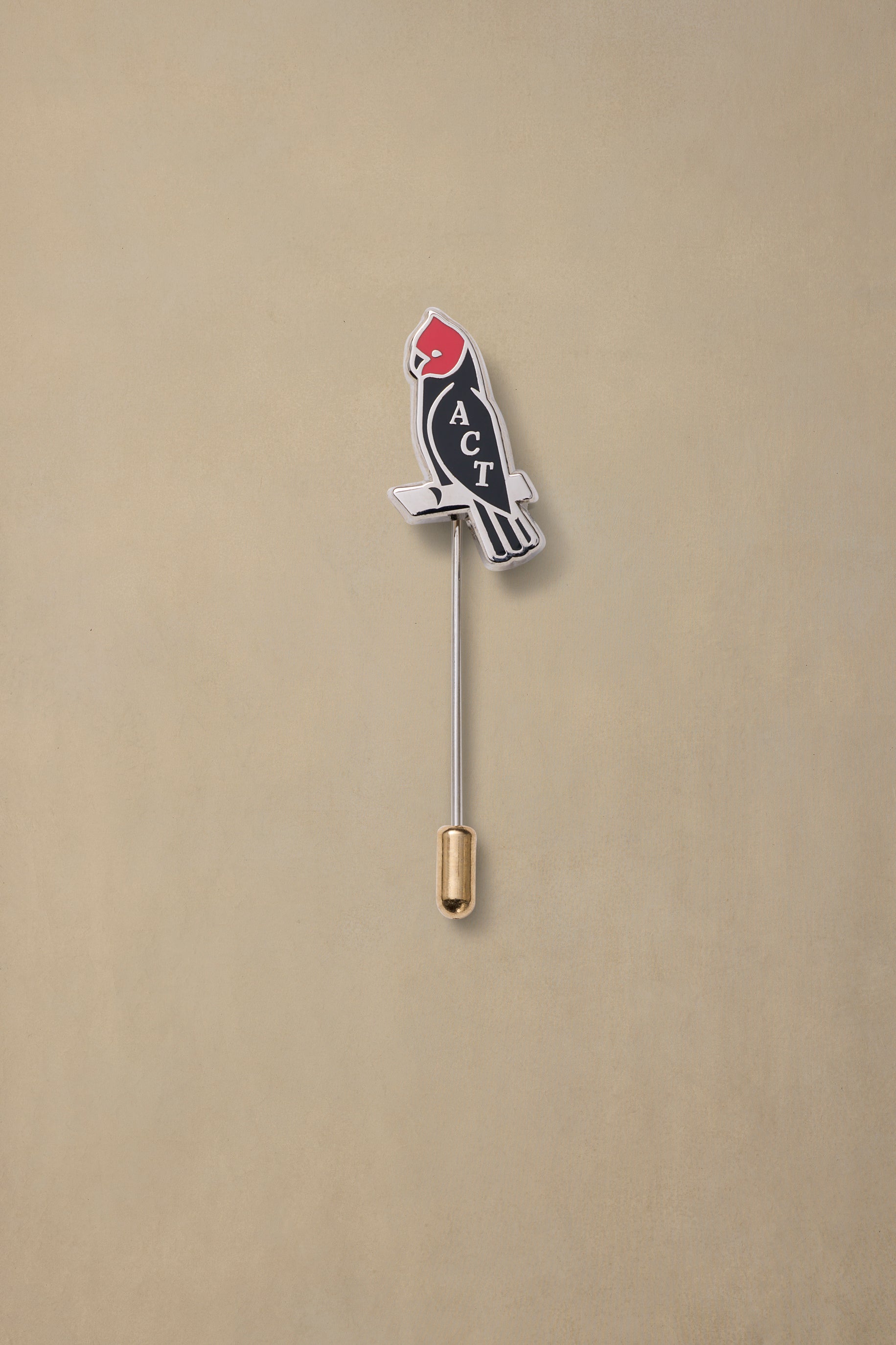 ACT State rocket pin with red nose cone and black body on gold clutch backing against beige background