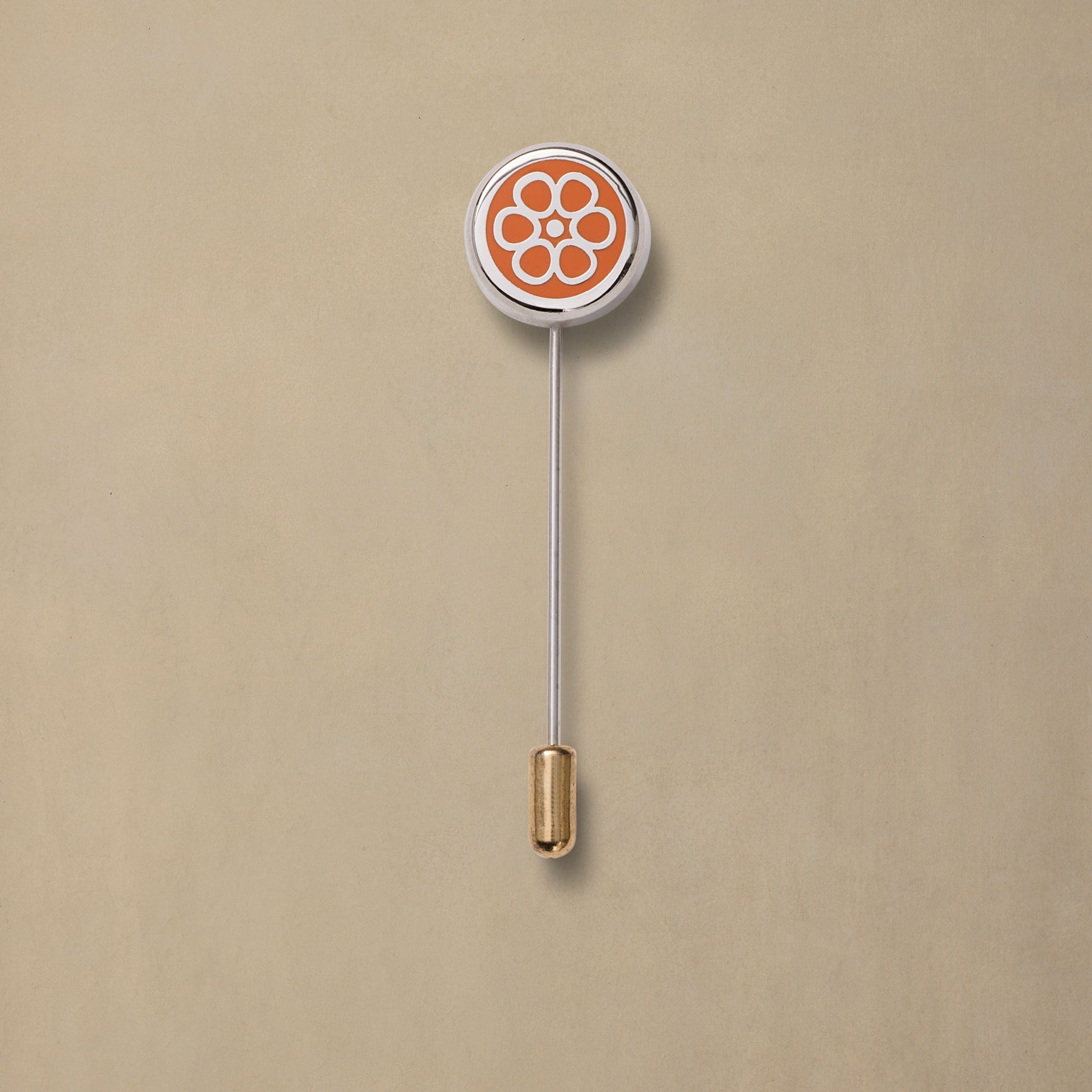 Orange and white enamel pin with floral design, silver stem, and gold-tone clutch backing on beige background