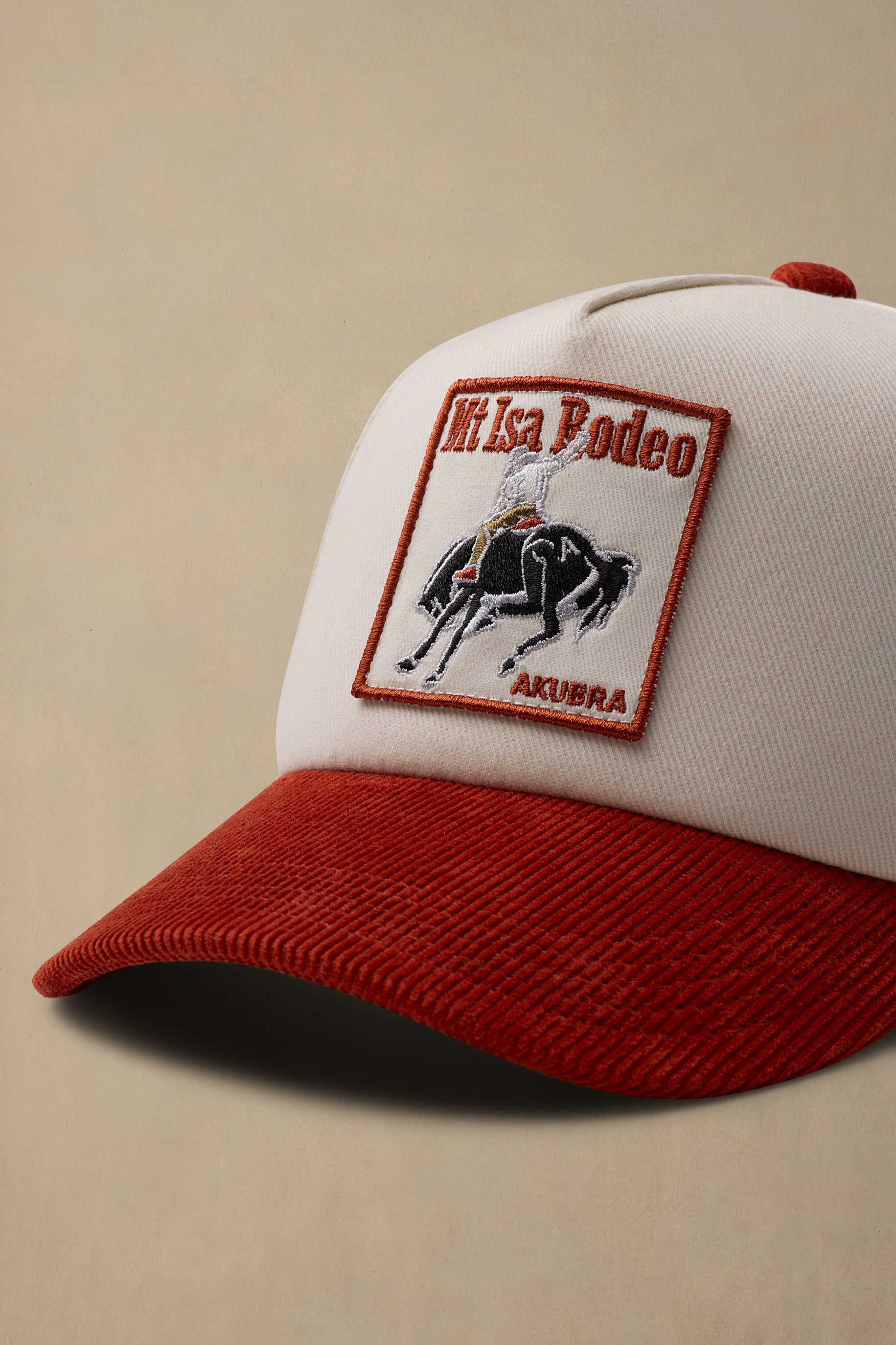 A close-up of a baseball cap with a white crown and a red curved brim. The front features an embroidered patch depicting a black horse with a rider and the text 'Mt Isa Rodeo'.