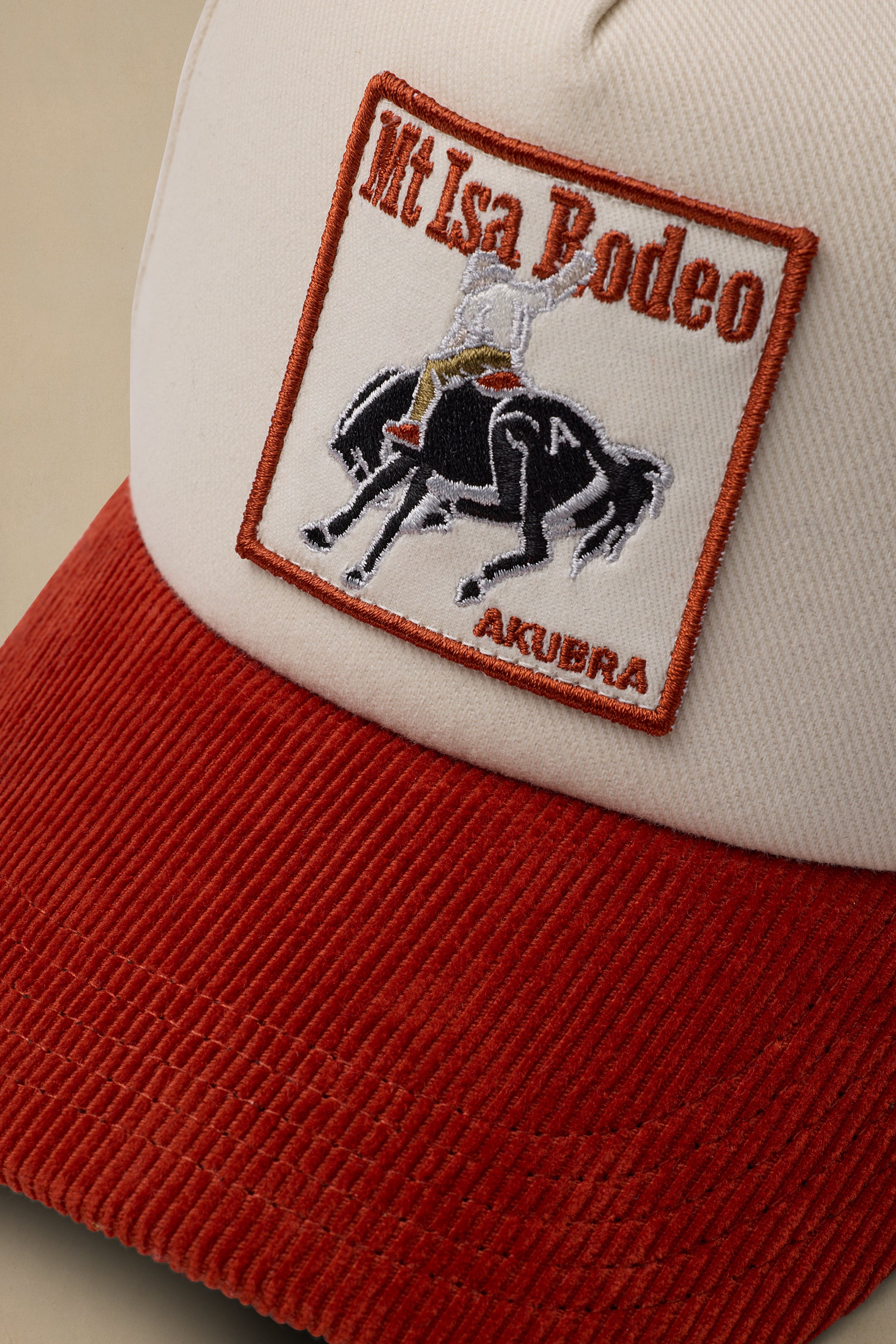 Close-up of a corduroy trucker hat with a cream crown and a red ribbed brim. The front patch reads "Mt Isa Rodeo" and "AKUBRA" with an embroidered rider on horseback.
