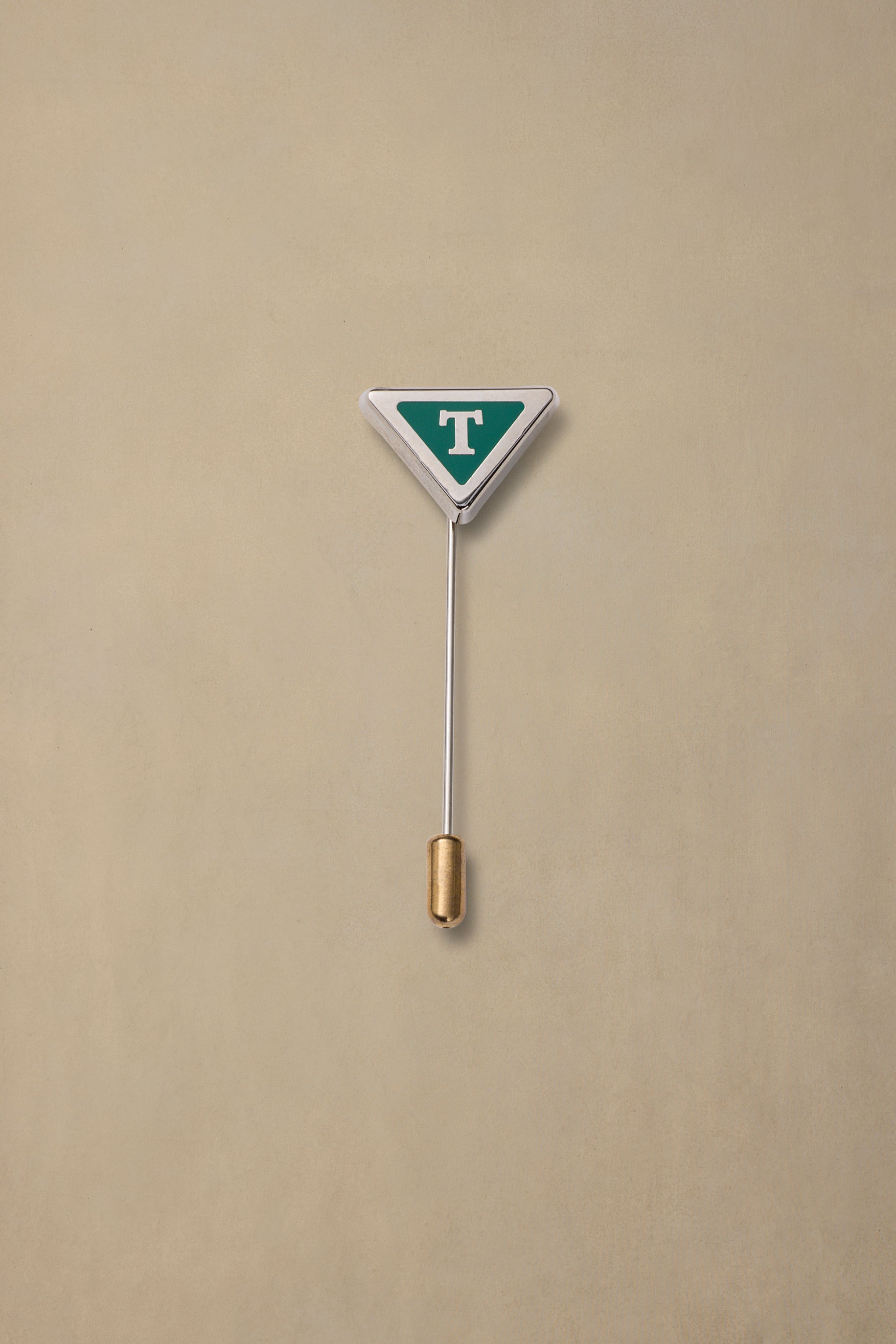 Green and white triangular Tasmania state pin with gold-tone clutch backing on beige background