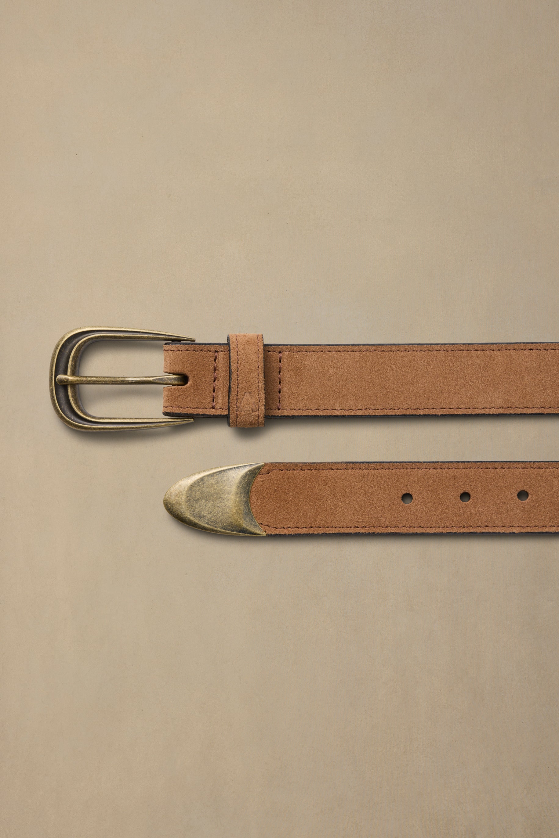 Tan suede belt with brass buckle and metal tip detail on neutral background