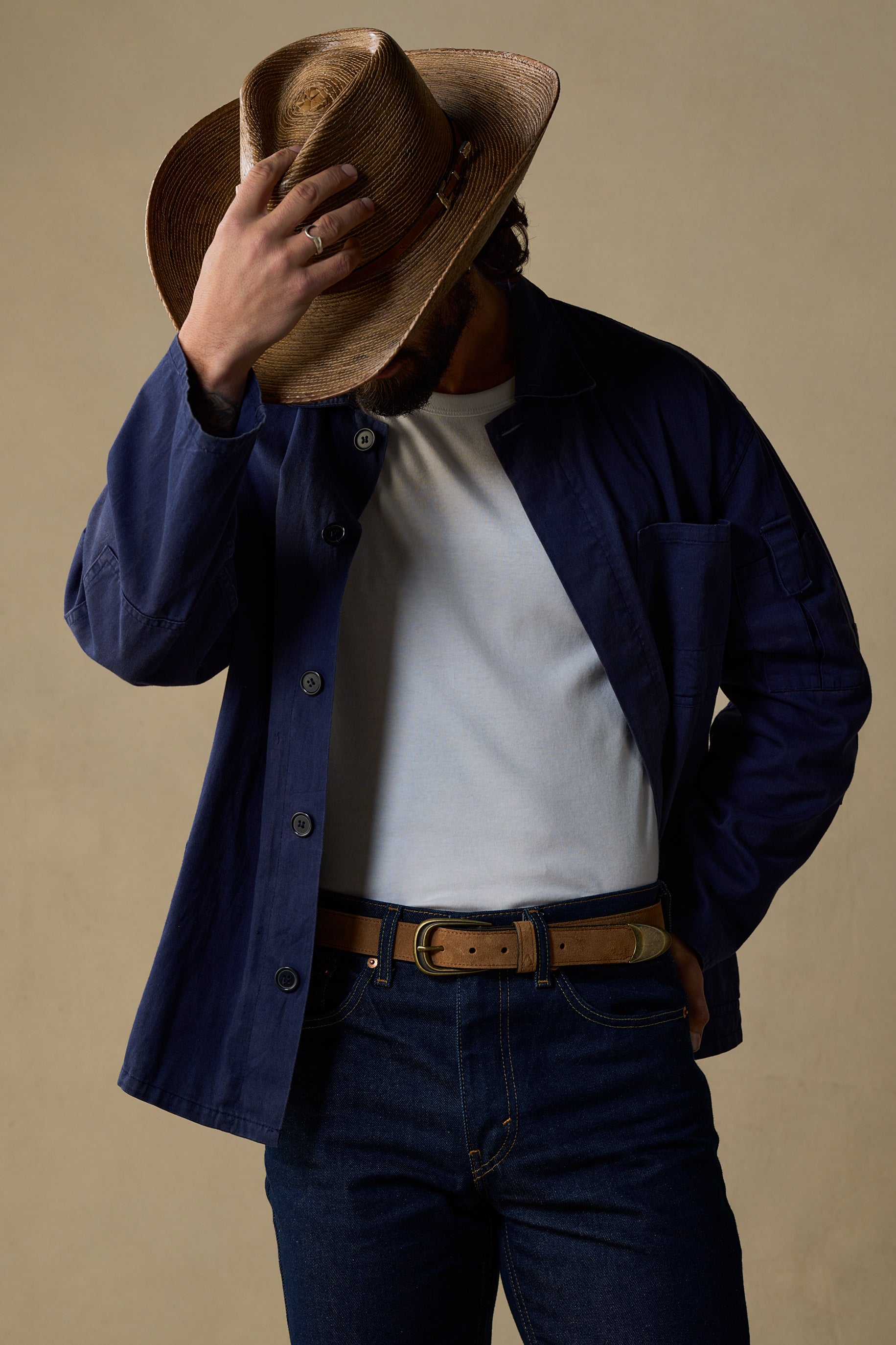 Tan suede belt with brass buckle worn with navy jacket and jeans against neutral background