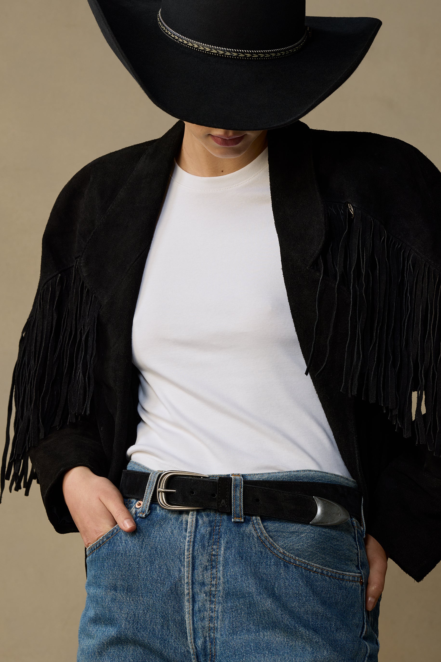 Black suede belt with pewter buckle worn with white tee, black fringed jacket, and blue jeans