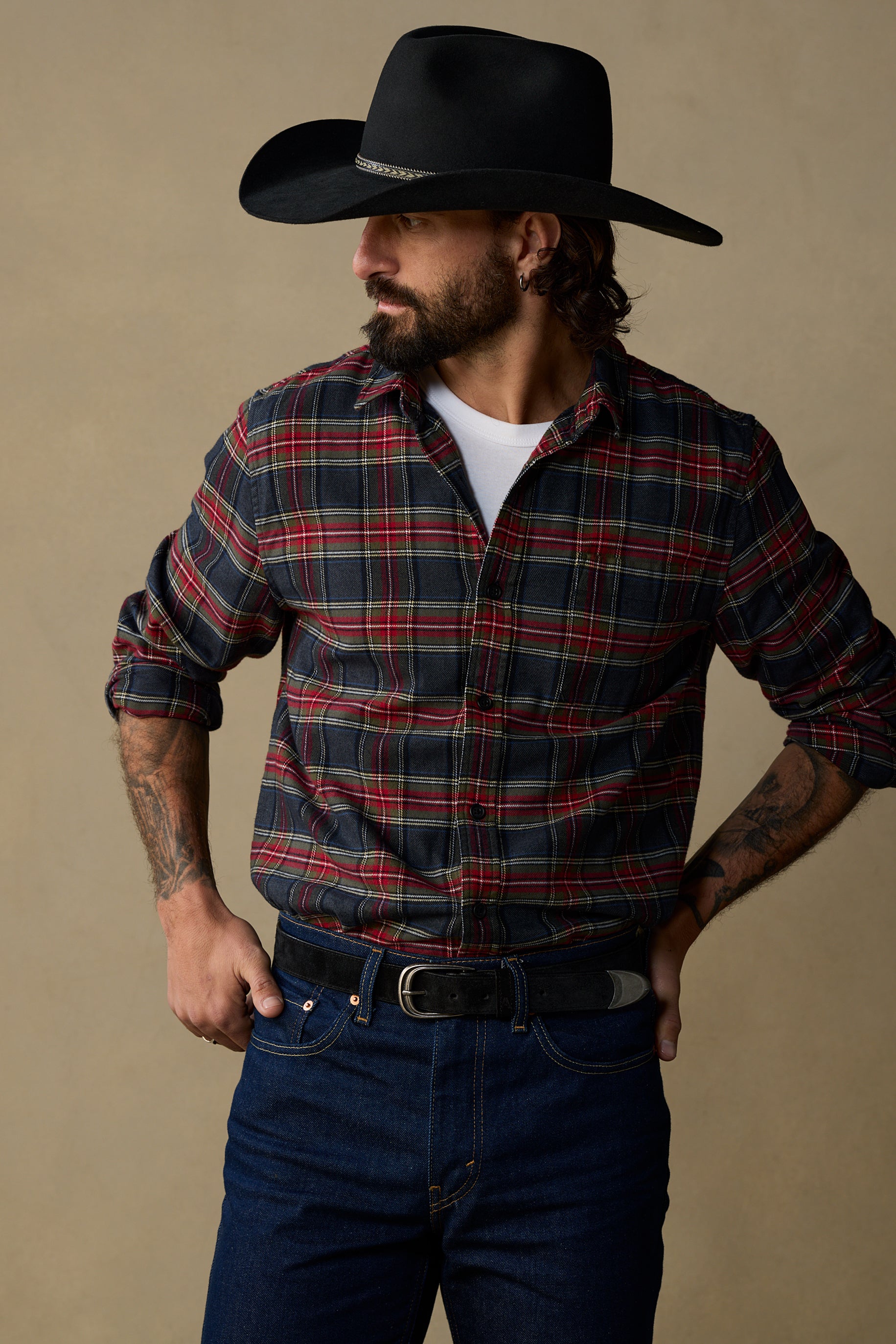 Black suede belt with pewter buckle worn with plaid shirt and jeans on beige background