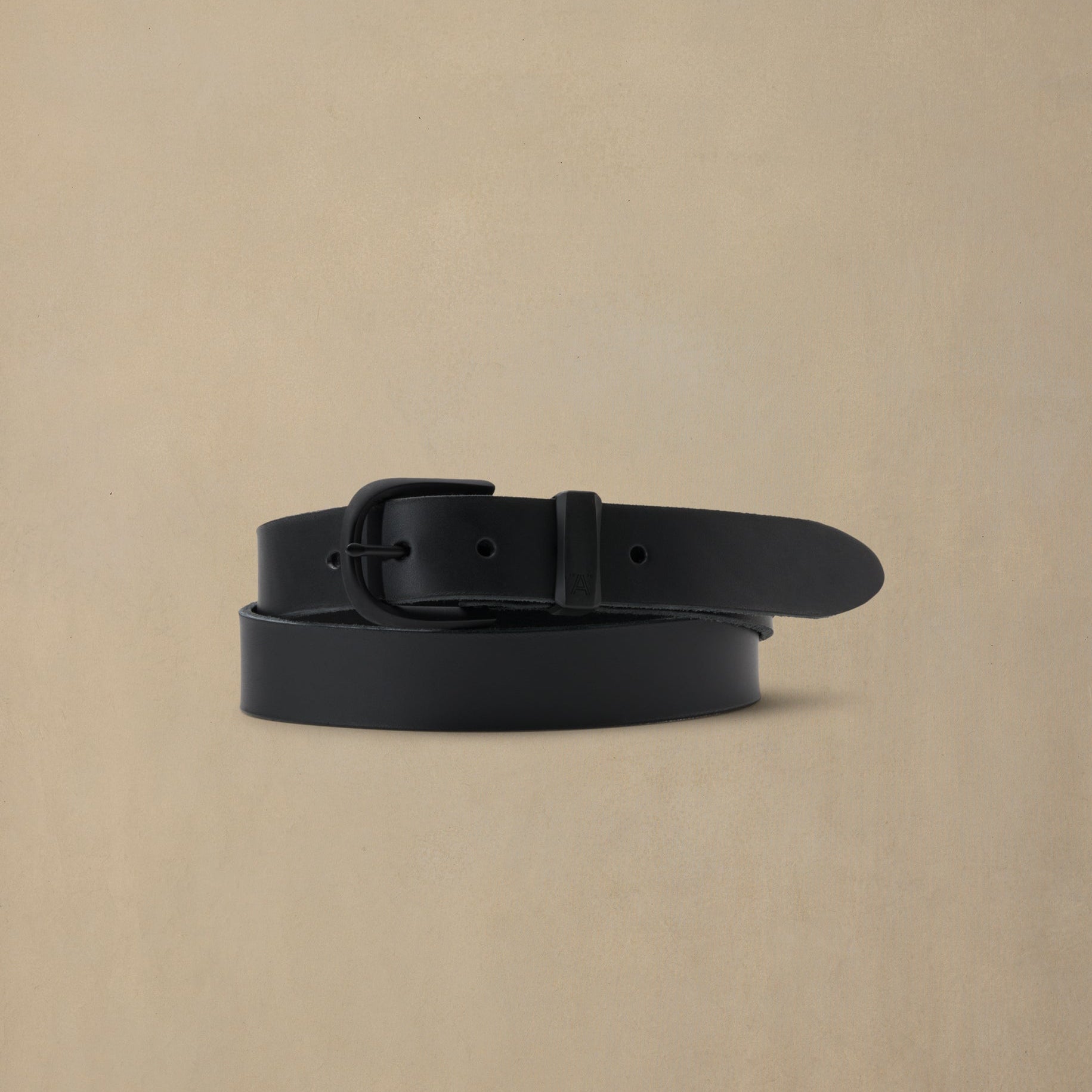 Black leather belt with black buckle on neutral beige background, coiled display view