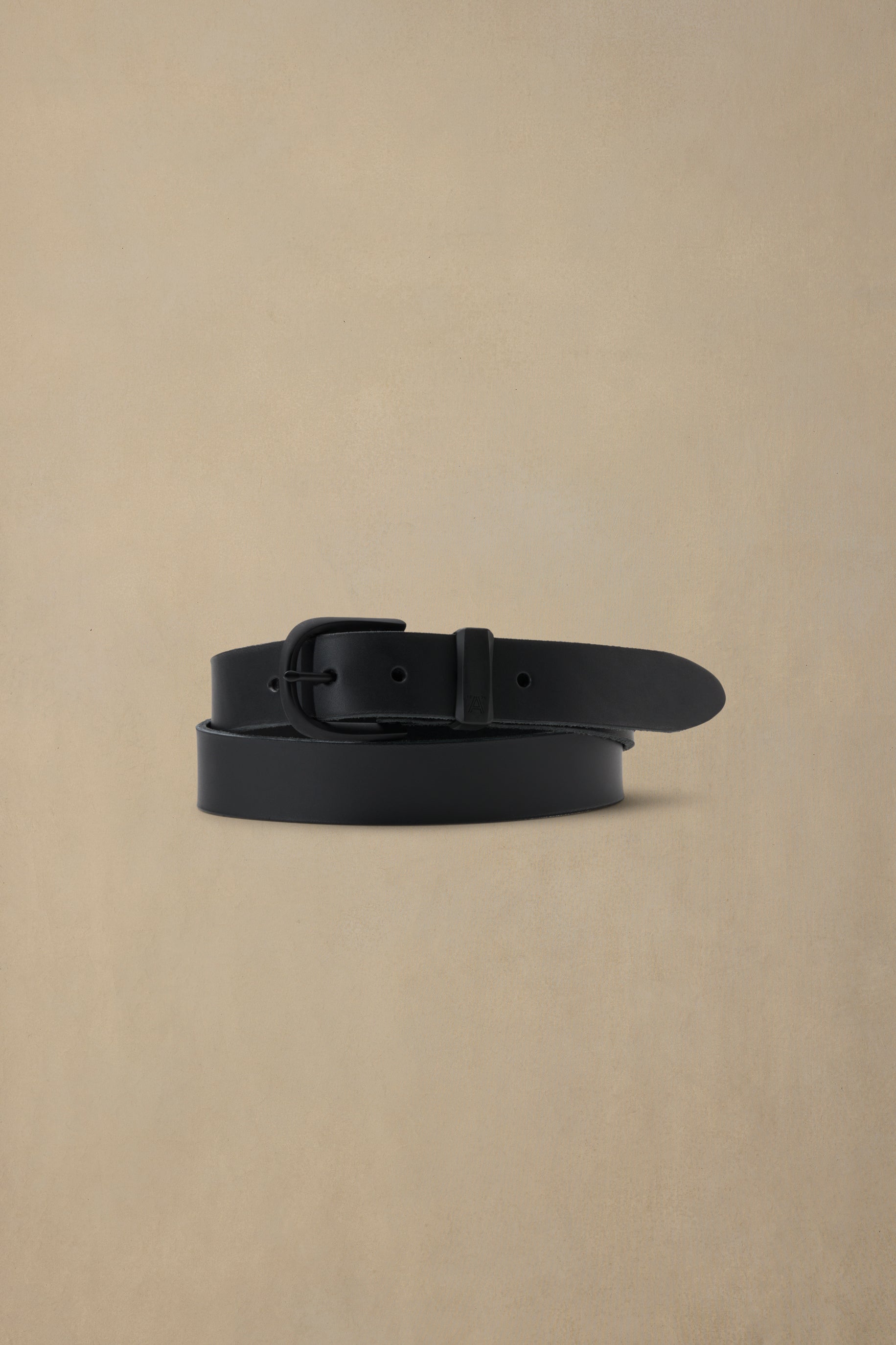 Black leather belt with black buckle on beige background, coiled display