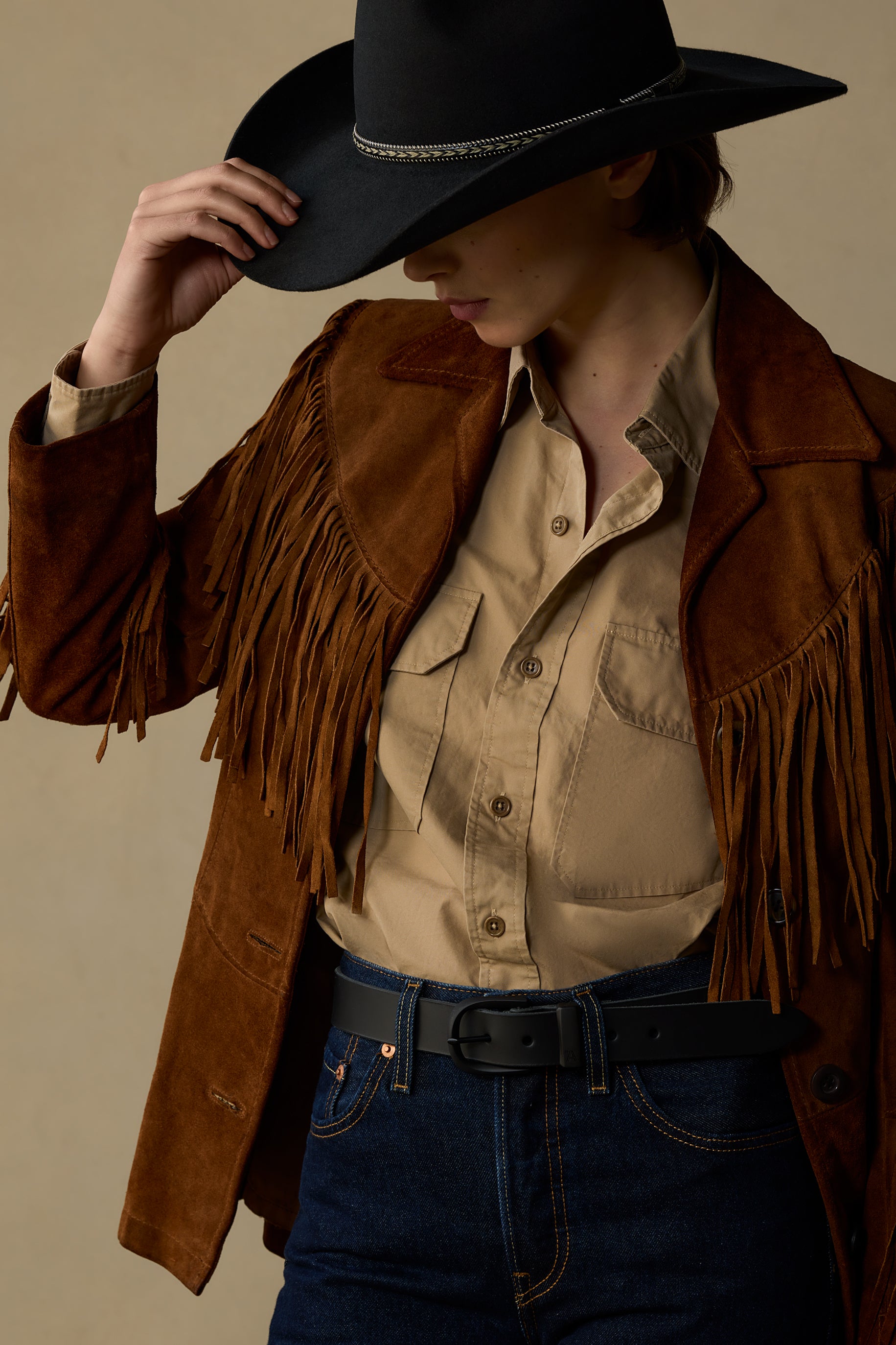Black leather belt with 30mm width worn with fringe suede jacket and cowboy hat on neutral background