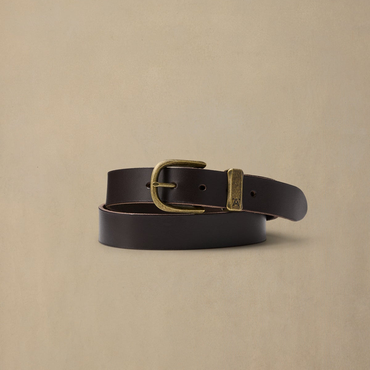 Dark brown leather belt with brass buckle and keeper loop on neutral beige background
