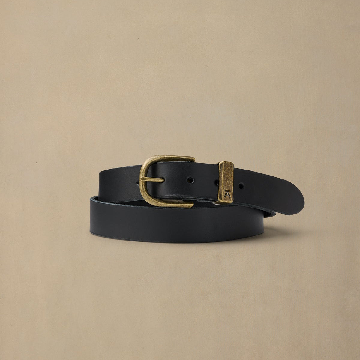 Black leather belt with brass buckle and keeper loop on neutral beige background