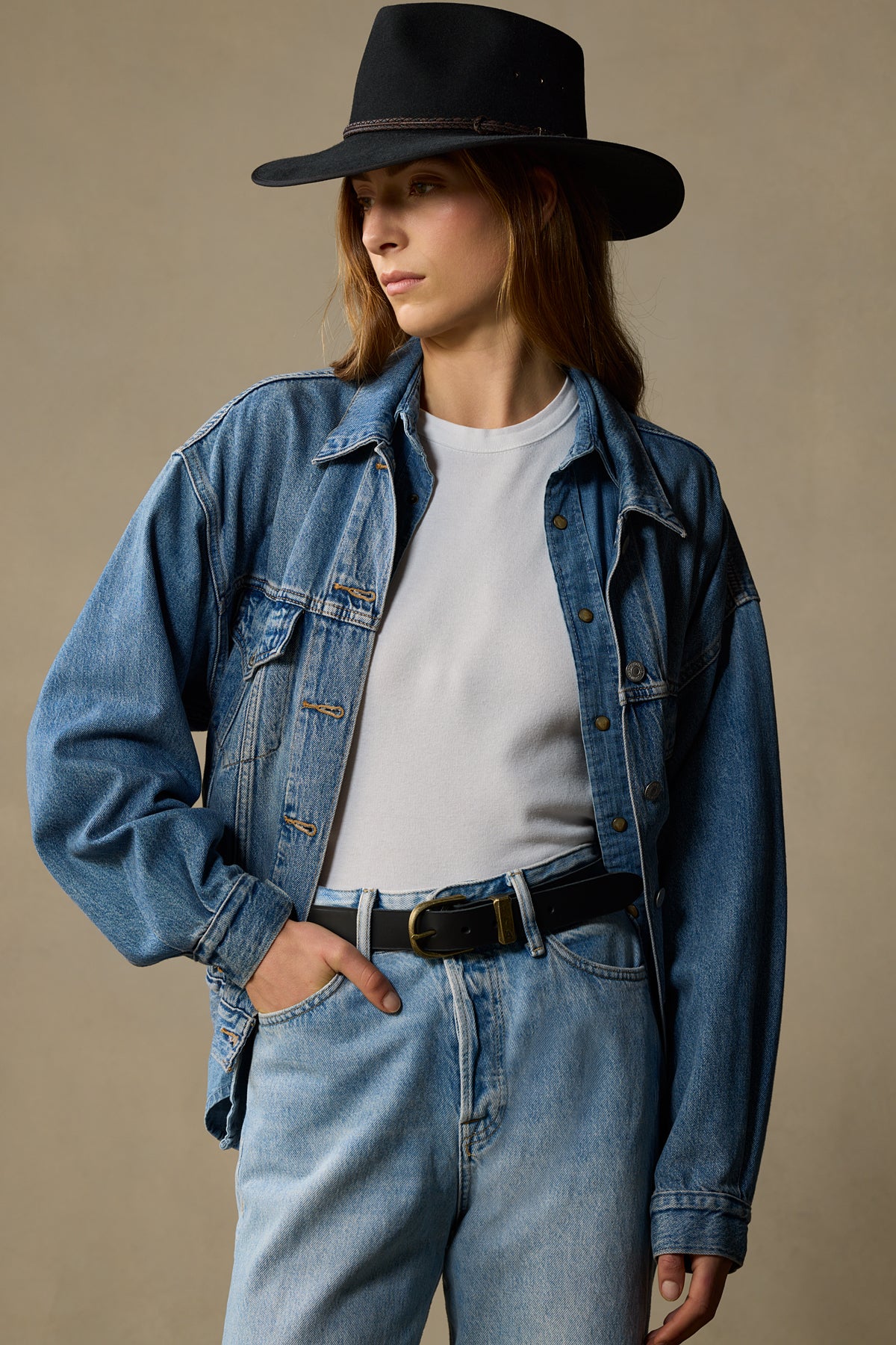 Black leather belt with brass buckle worn with denim jacket and jeans on model against neutral background