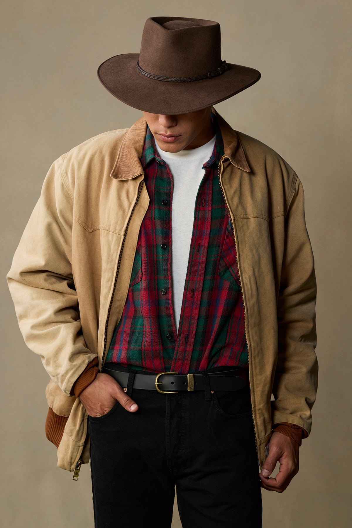 Black leather belt with brass buckle worn on model in tan jacket and plaid shirt