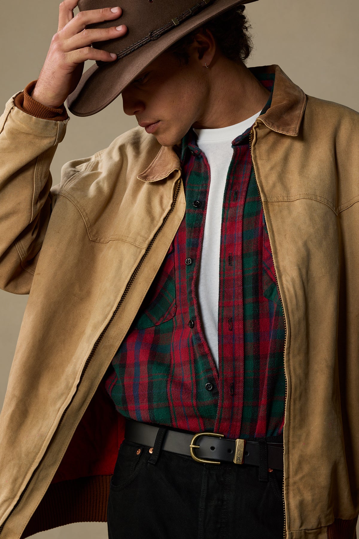 Black leather belt with brass buckle worn with tan jacket and plaid shirt