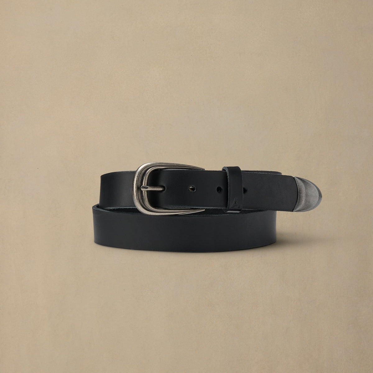 Black leather belt with silver pewter buckle on neutral beige background