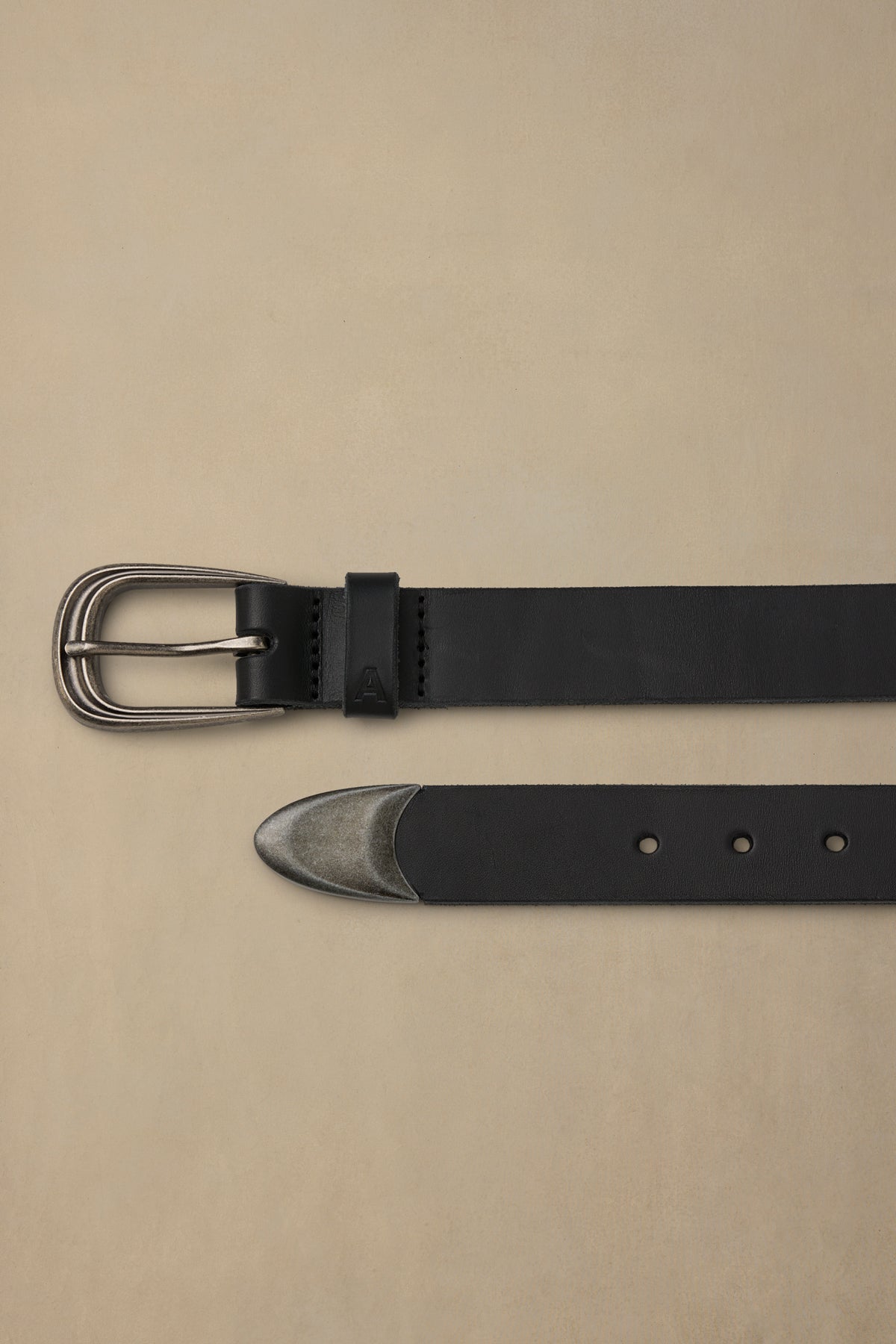 Black leather belt with pewter buckle and metal tip detail against neutral background
