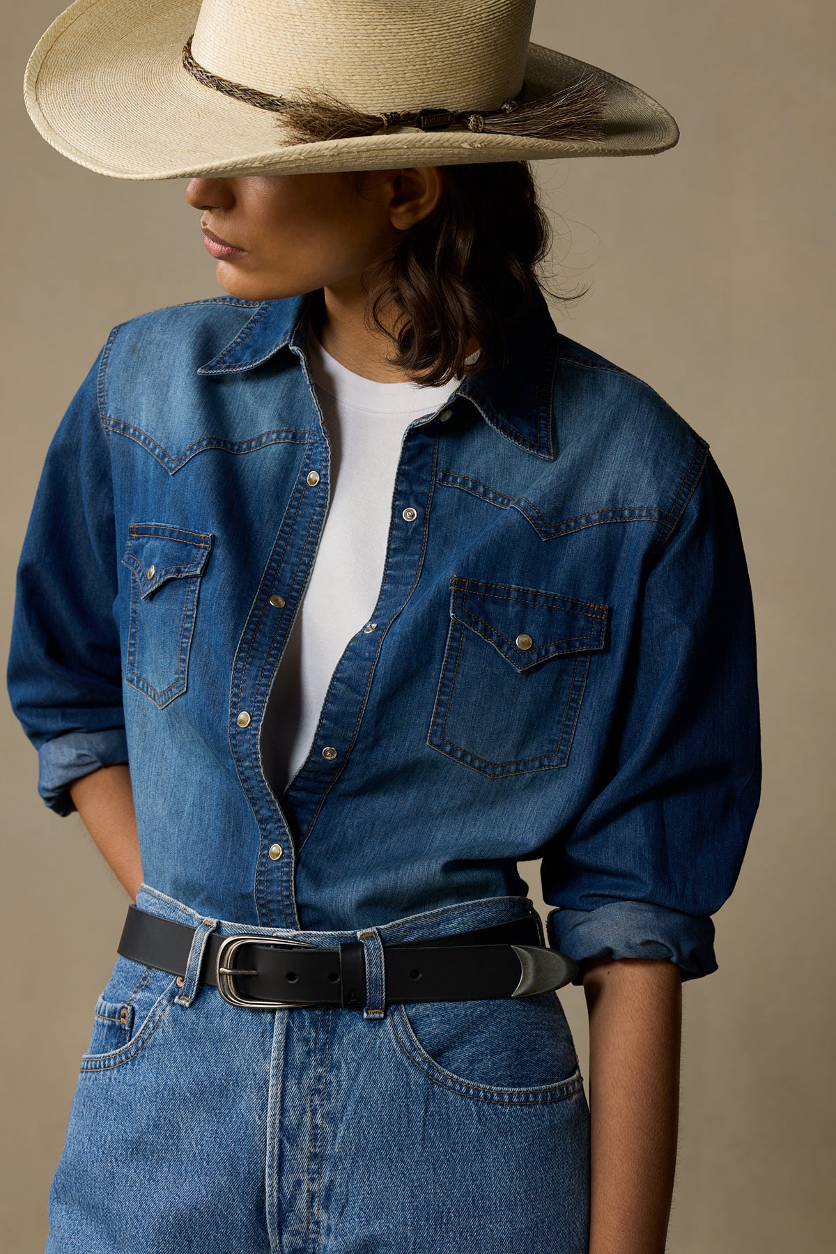 Black leather belt with silver buckle worn with denim shirt and cowboy hat on neutral background