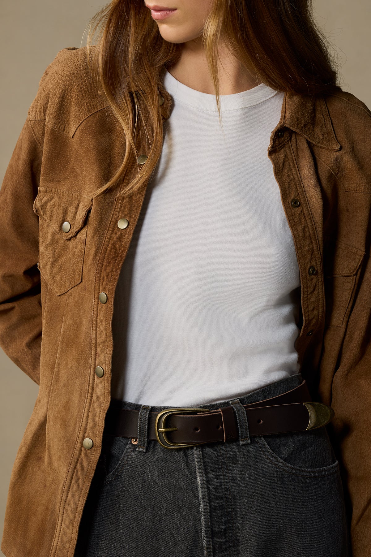 Brown leather belt with brass buckle worn with white tee and denim, styled on model