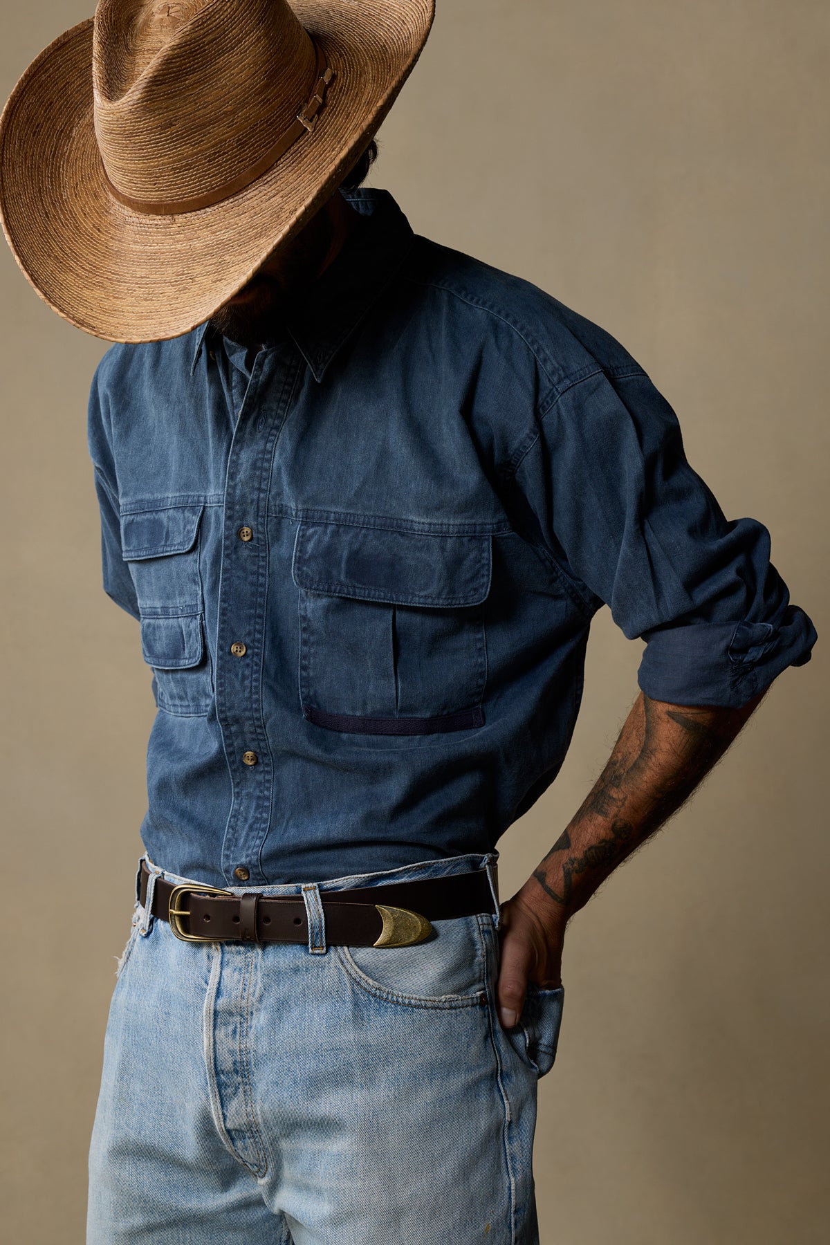 Brown leather belt with brass buckle worn with denim shirt and light jeans, styled with straw cowboy hat