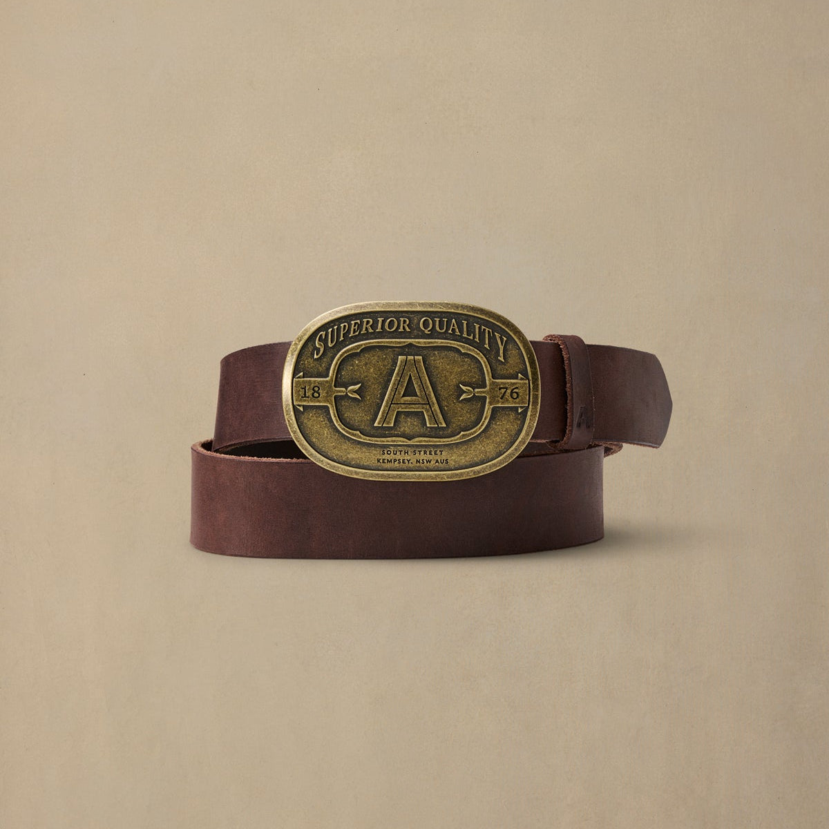Chocolate brown leather belt with brass "Superior Quality" buckle featuring "A" initial and 1876 date stamp, displayed against neutral background