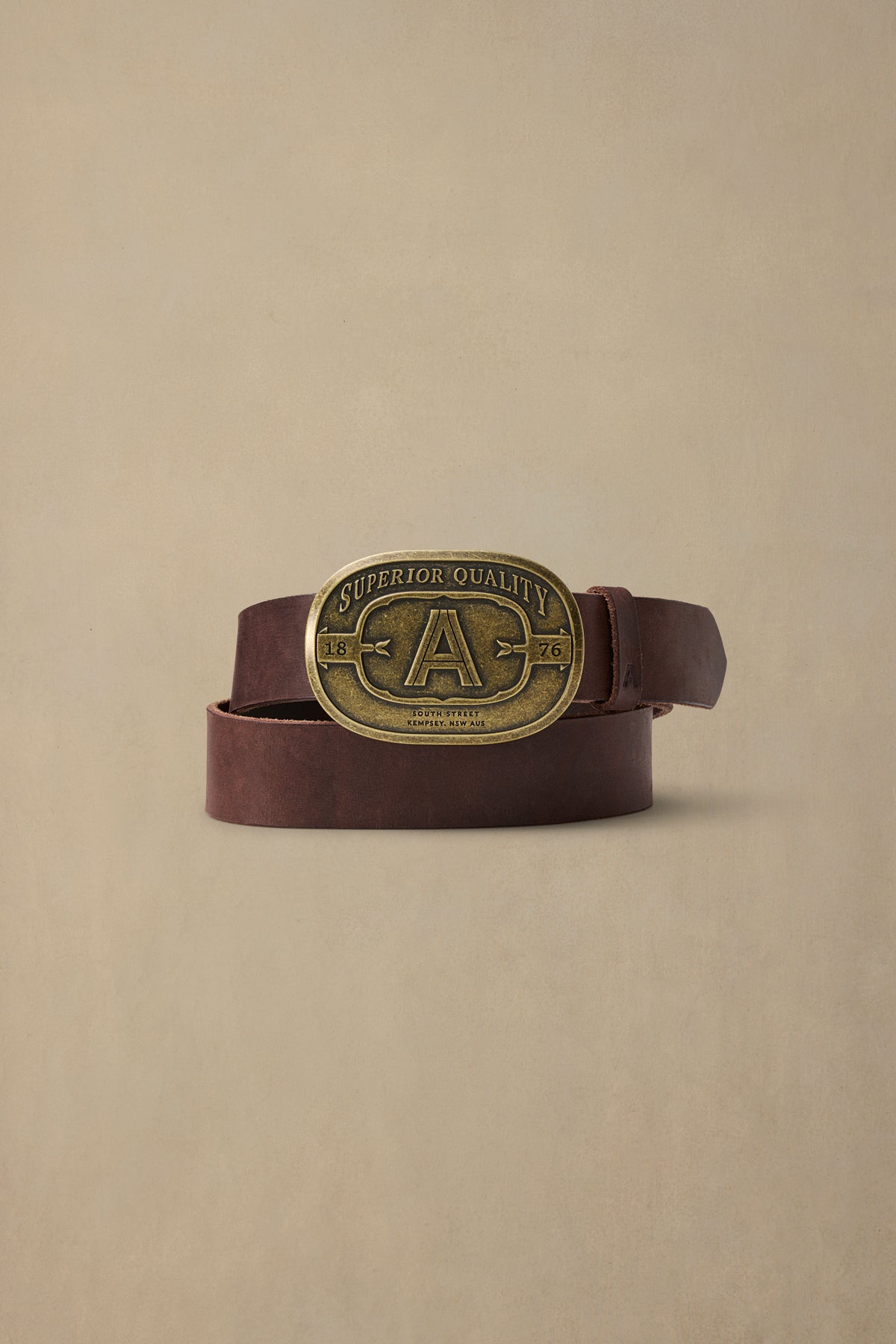 Brown leather belt with vintage brass buckle featuring "Superior Quality" text and 1876 date stamp on neutral background